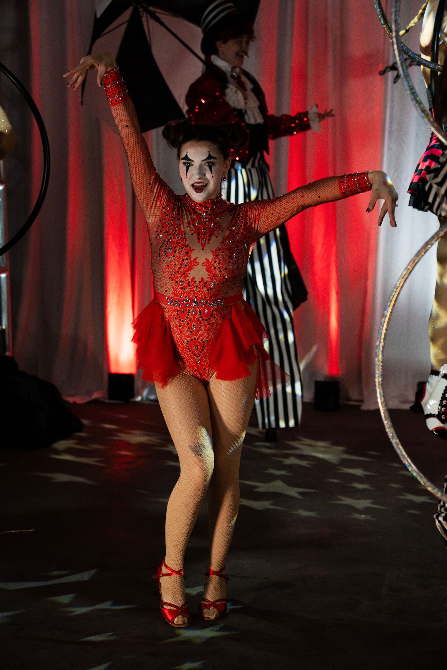 Female circus performer in red sequin costume with mime makeup dancing on a star-lit stage.
