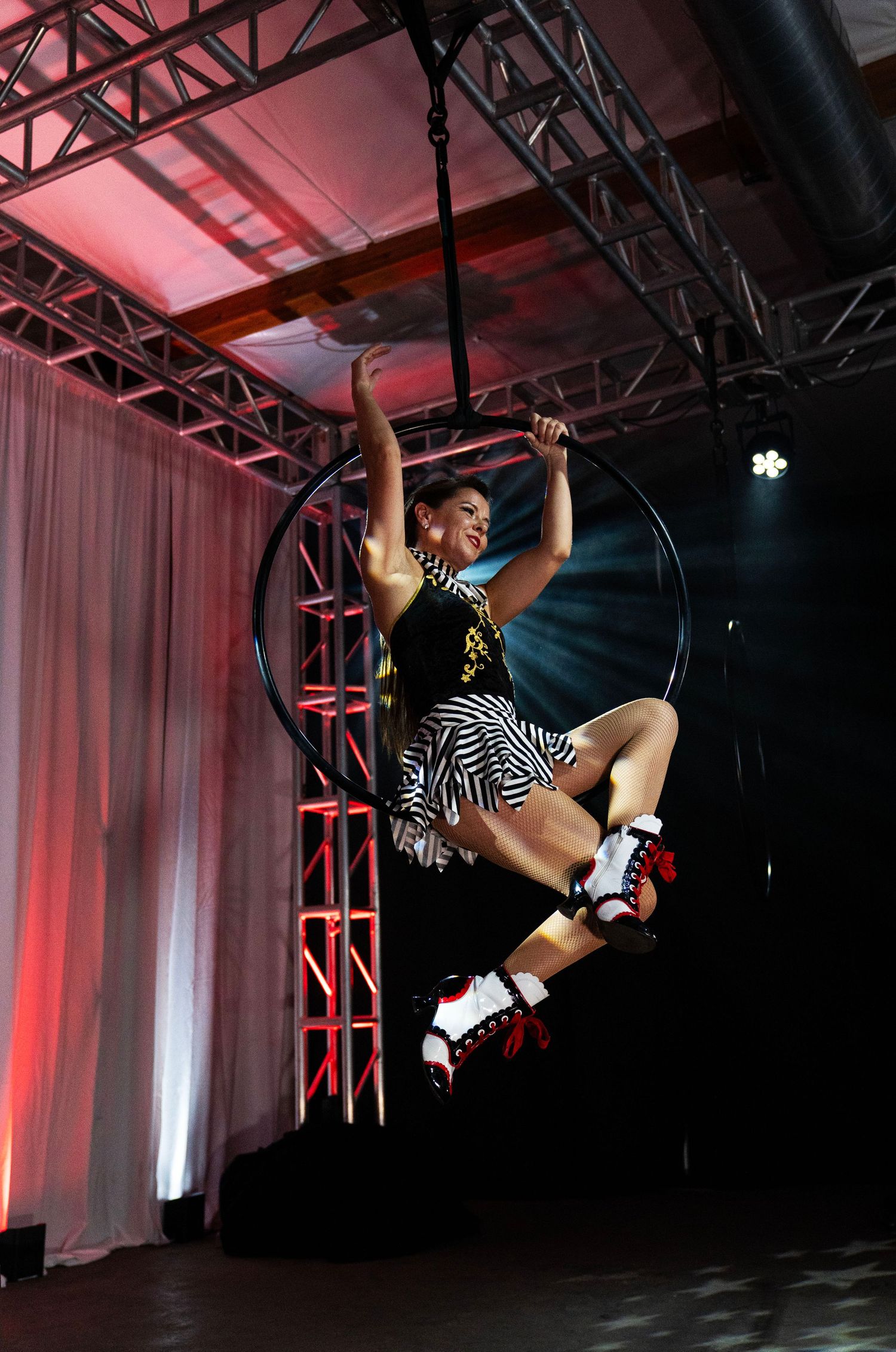 Aerial hoop performer in circus costume with roller skates executing dynamic moves on lyra at indoor event. Circus Photoshoot
