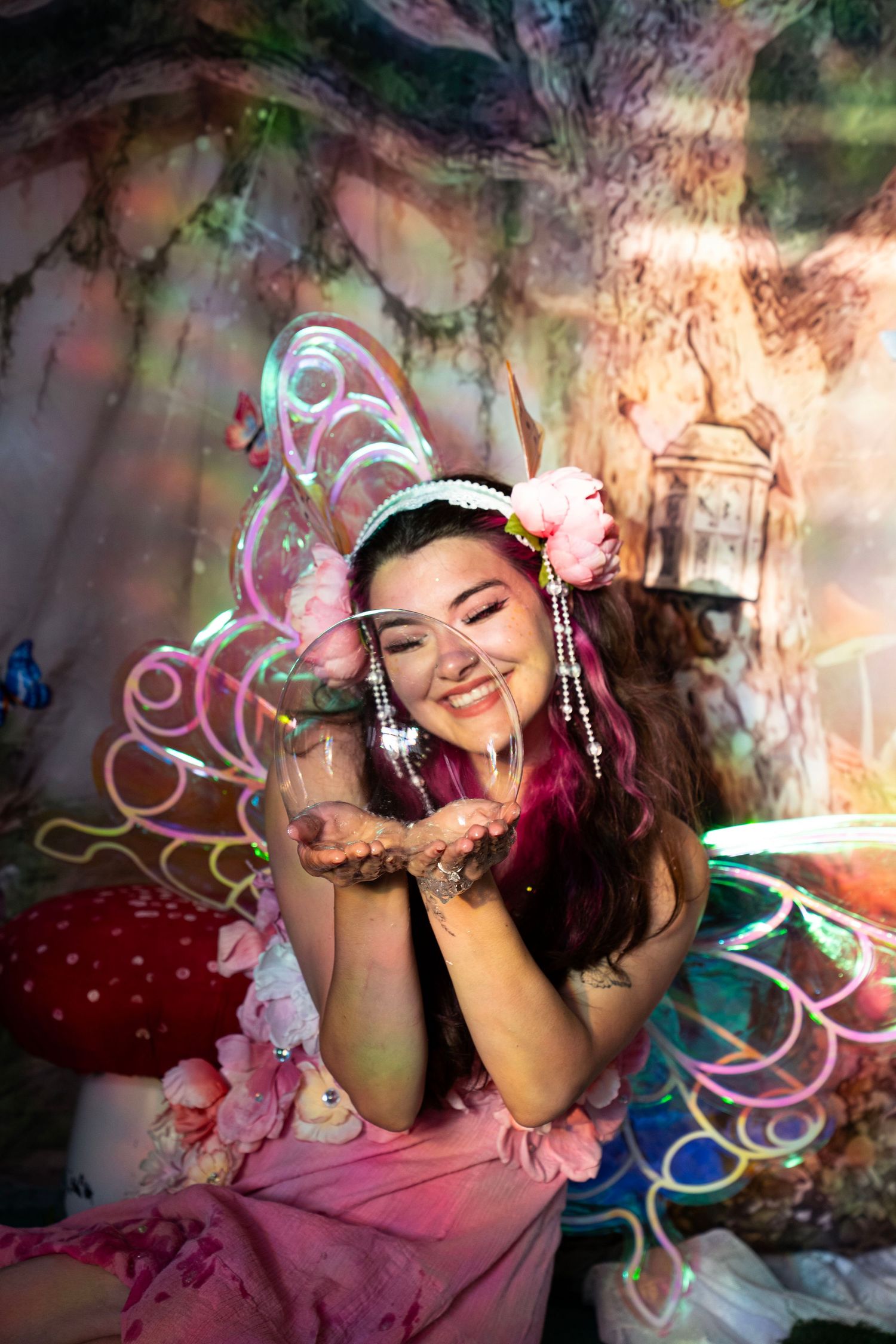 Woman in fairy costume blows glitter from her hands wearing LED wings in an enchanted forest studio. Fantasy Photoshoot