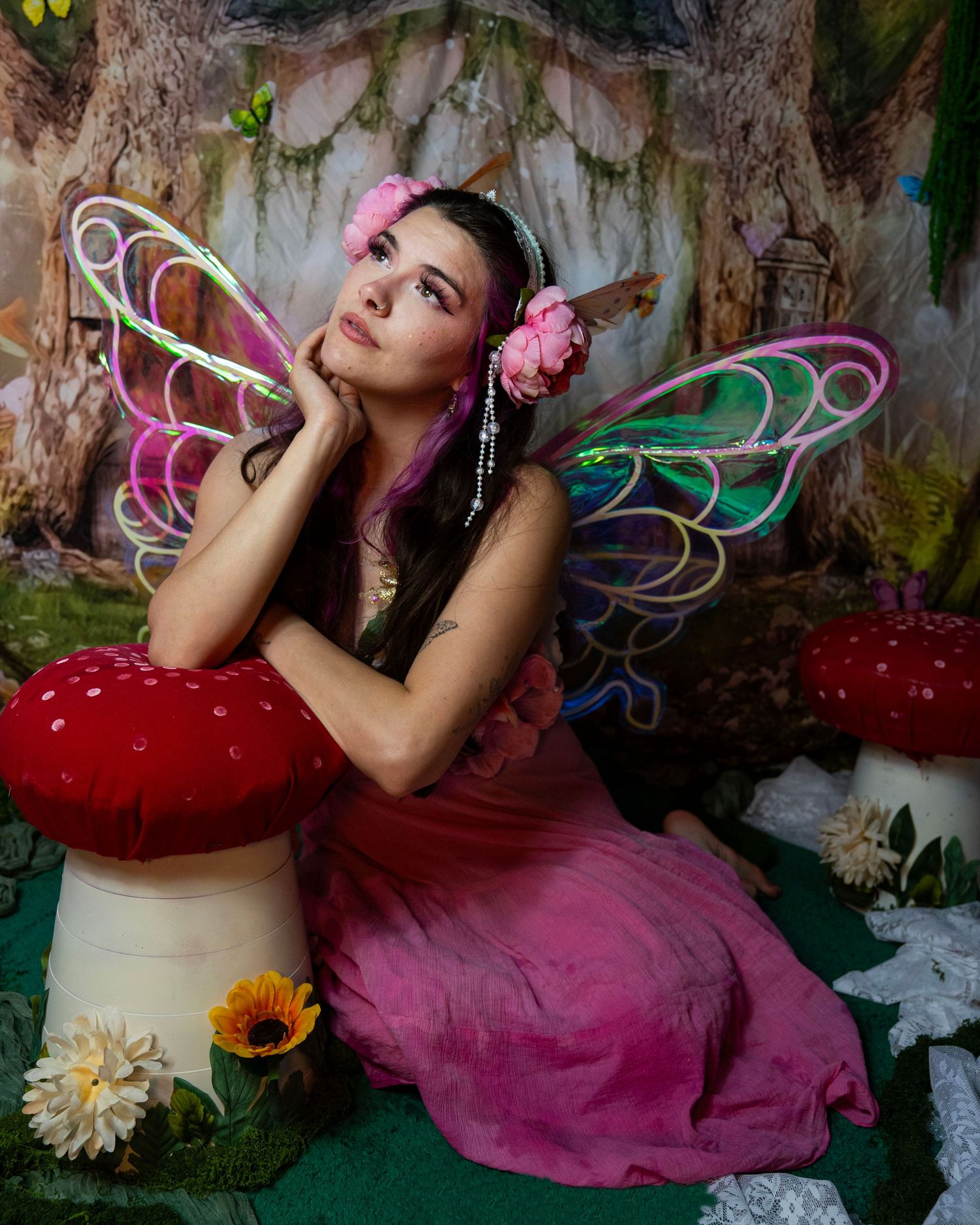 Woman in pink fairy costume with colorful wings poses in enchanted forest setting. Fantasy Photoshoot