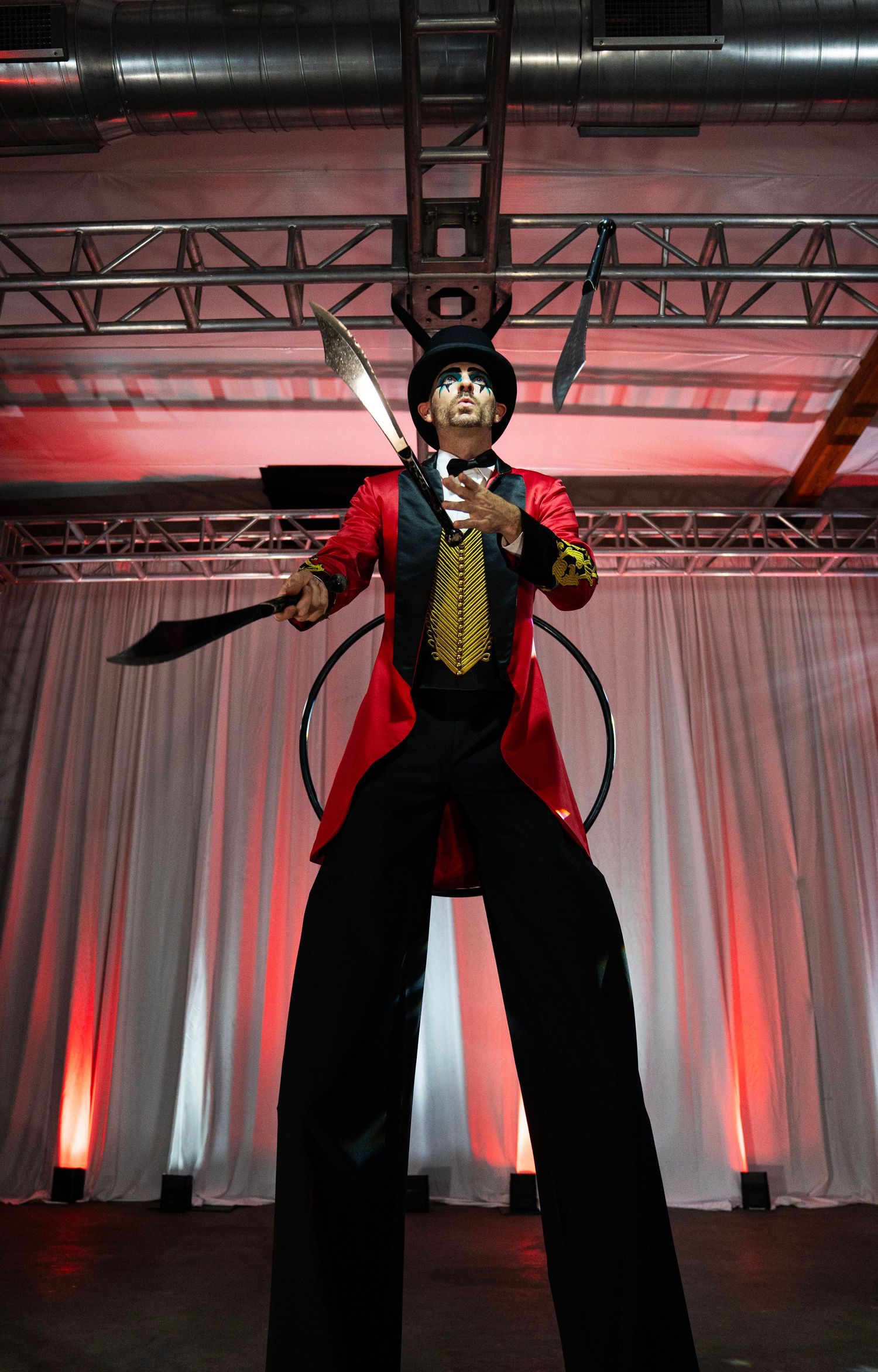 Circus ringmaster on stilts in red tailcoat and top hat juggling swords and hoops on a dramatic stage. Circus Photoshoot