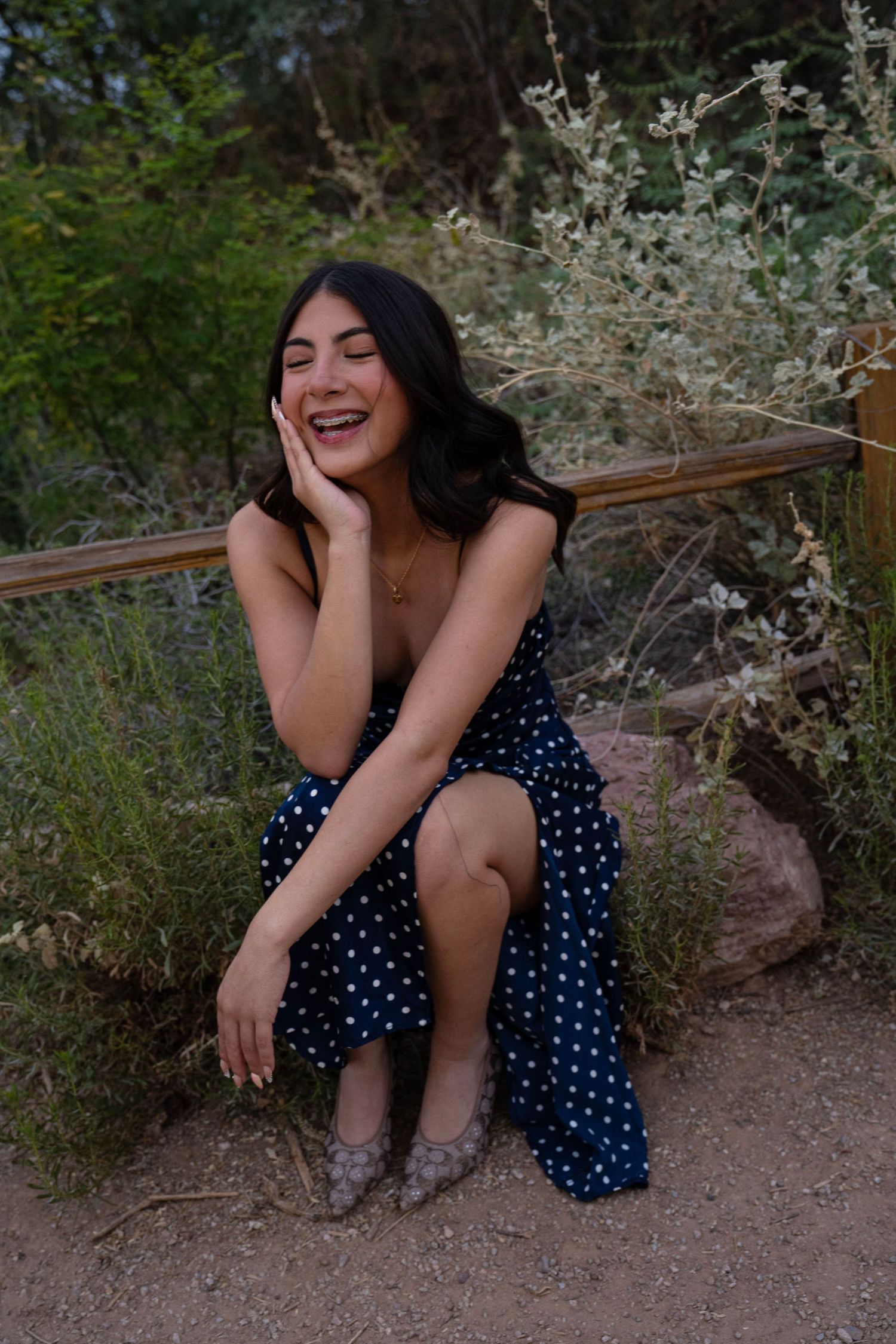 Happy young woman in polka dot dress sitting on rock laughing outdoors.