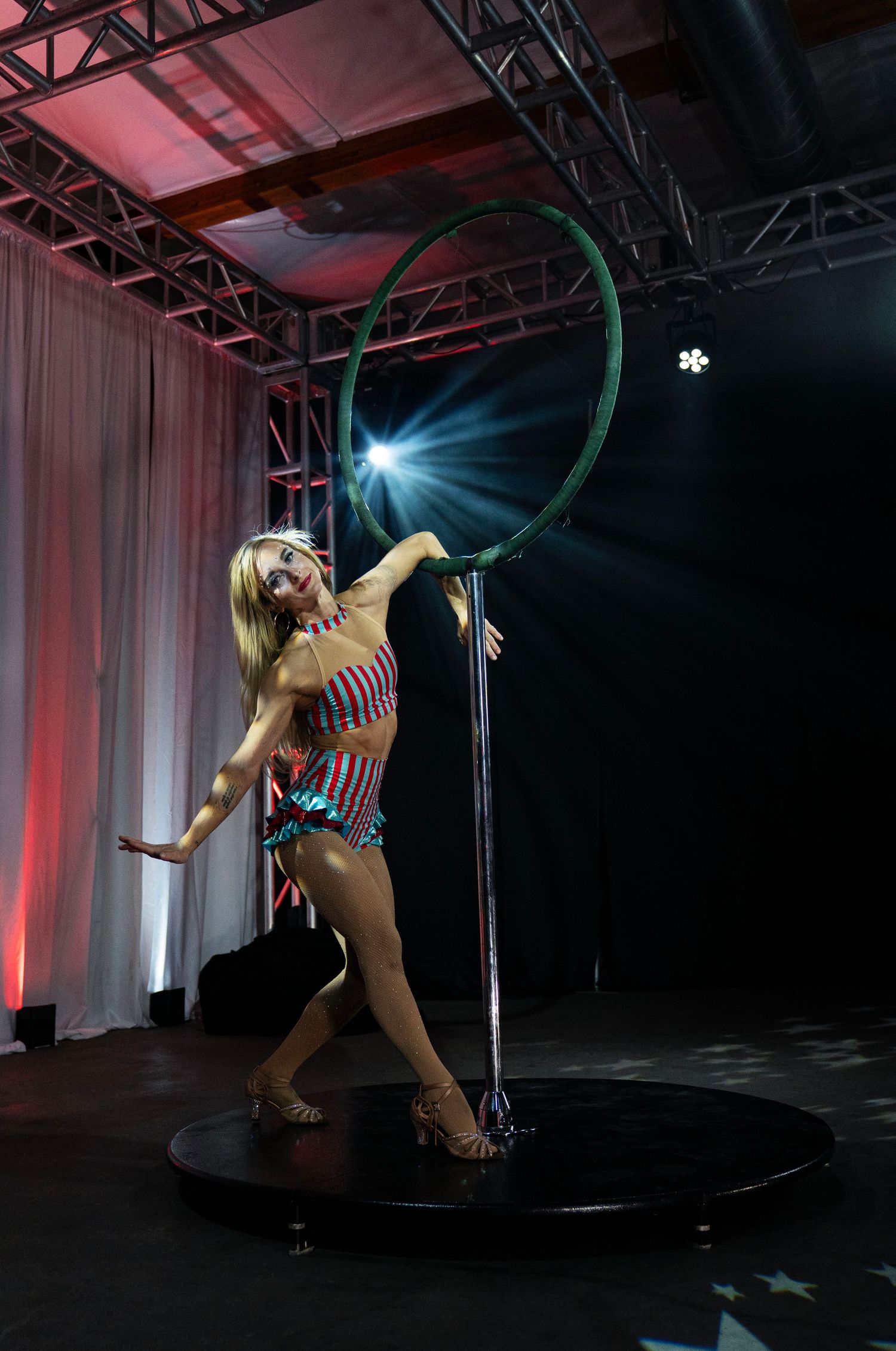 Blonde performer in patriotic costume poses with large green hoop on circular stage platform. Circus Photoshoot
