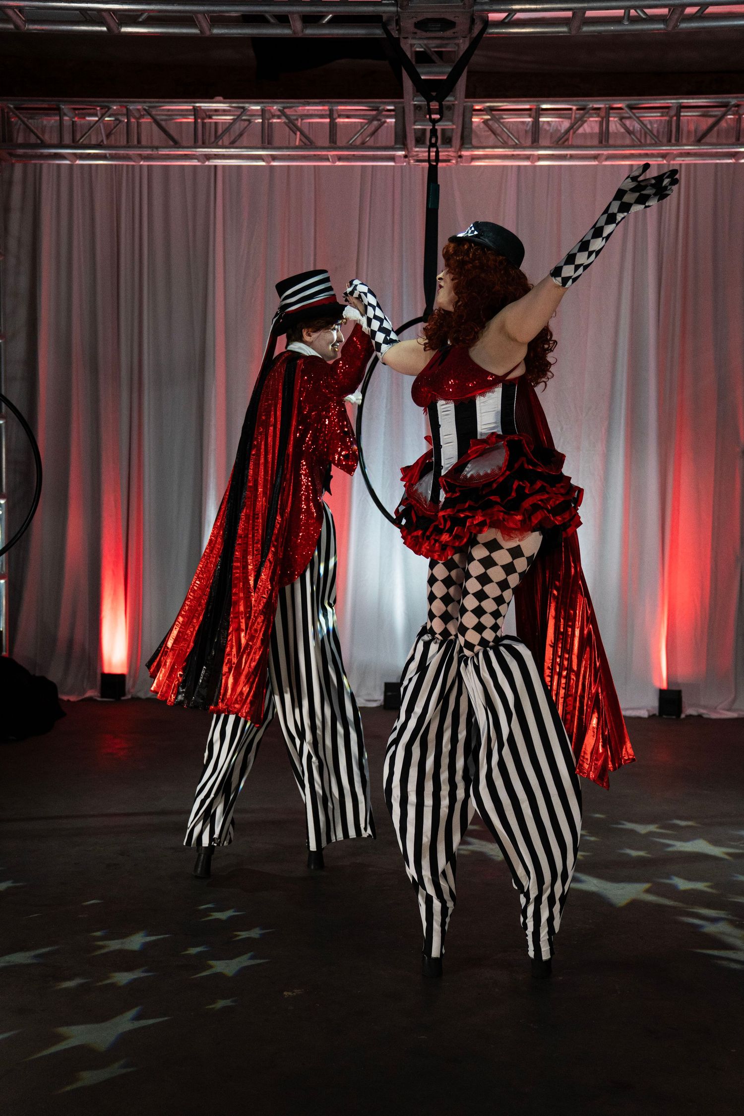 Two circus stilt walkers in red and black costumes perform together at themed event.