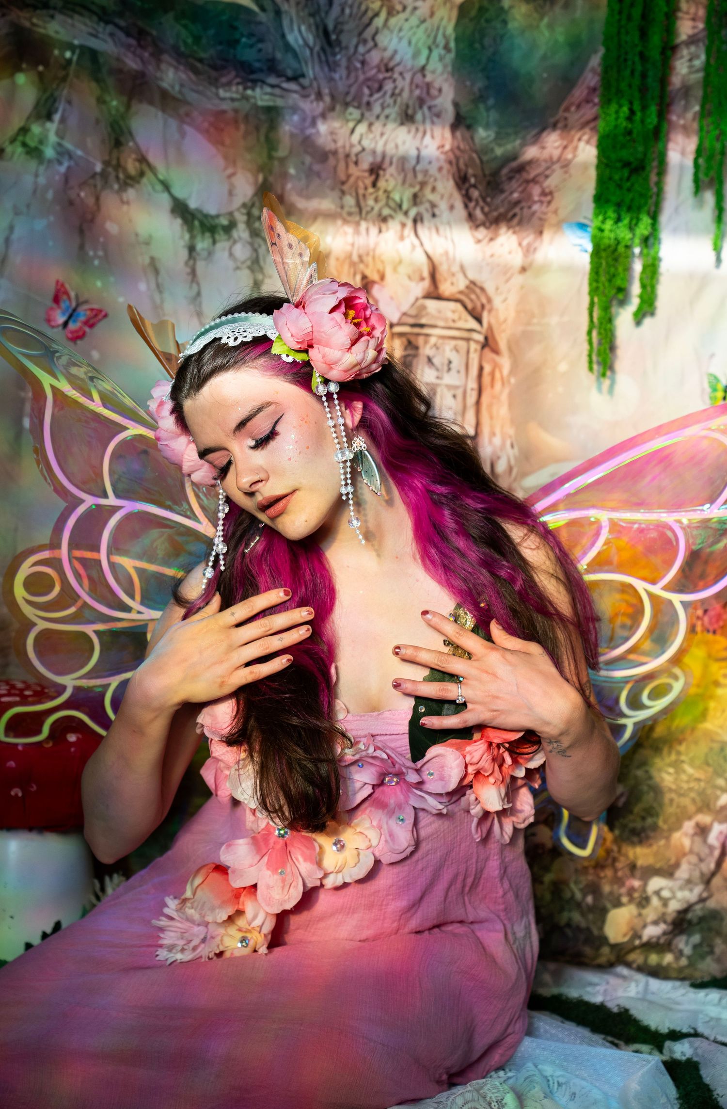 Woman in fairy costume with pink flowers and butterfly wings in an enchanted forest studio. Fantasy Photoshoot