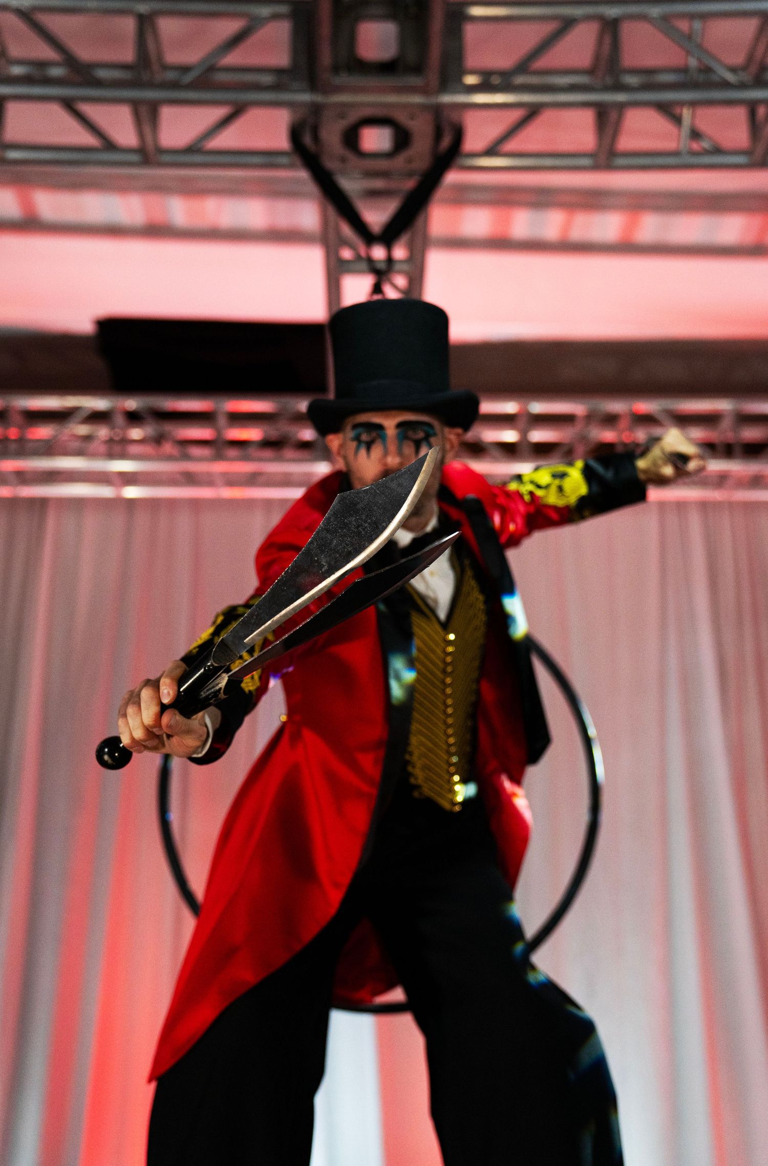 Dramatic circus ringmaster in red tailcoat and top hat poses with ornate sword on stilts. Circus Photoshoot