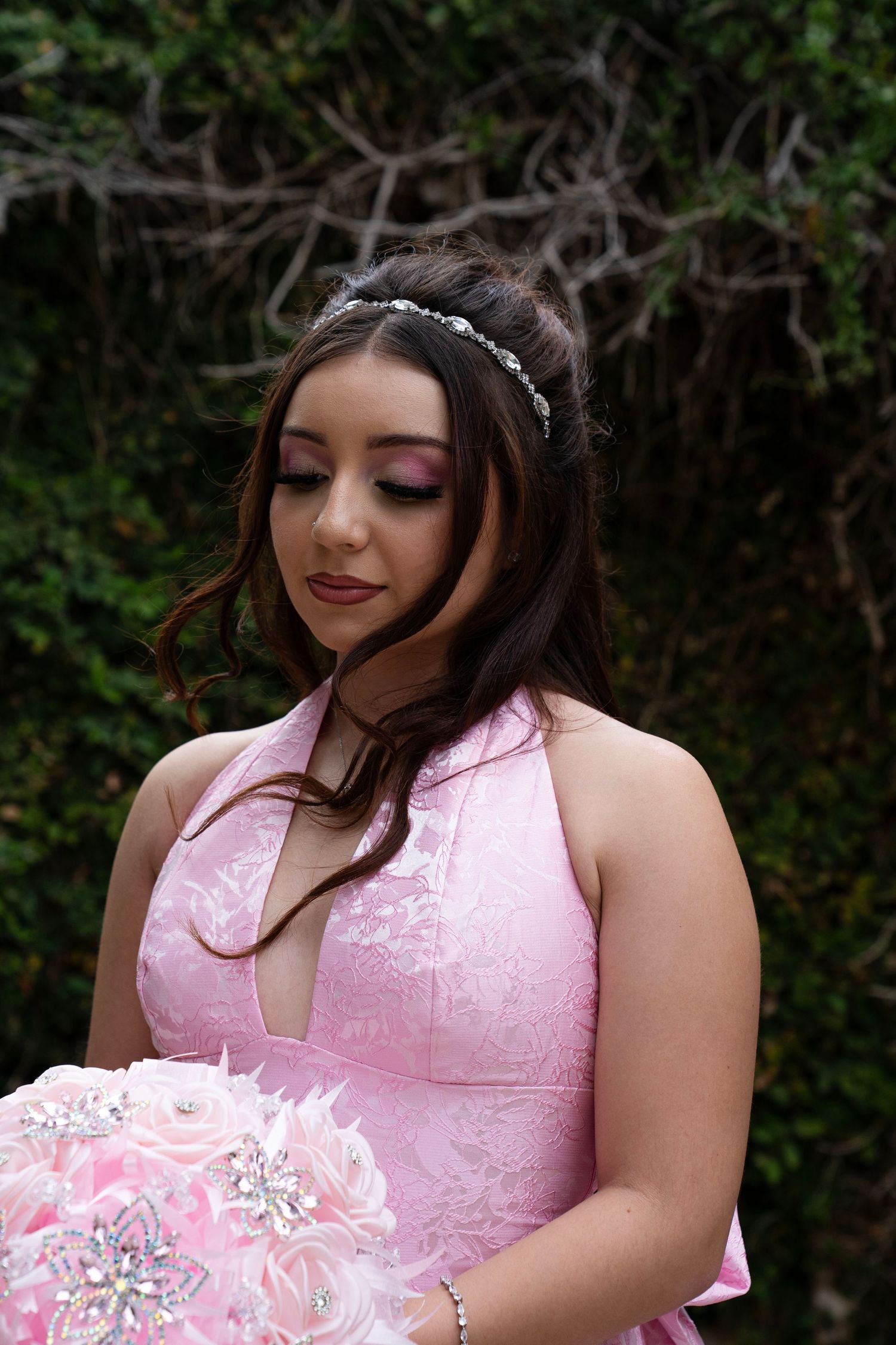 Close-up of woman in pink halter dress with rhinestone headband holding a pink feather and brooch bouquet.