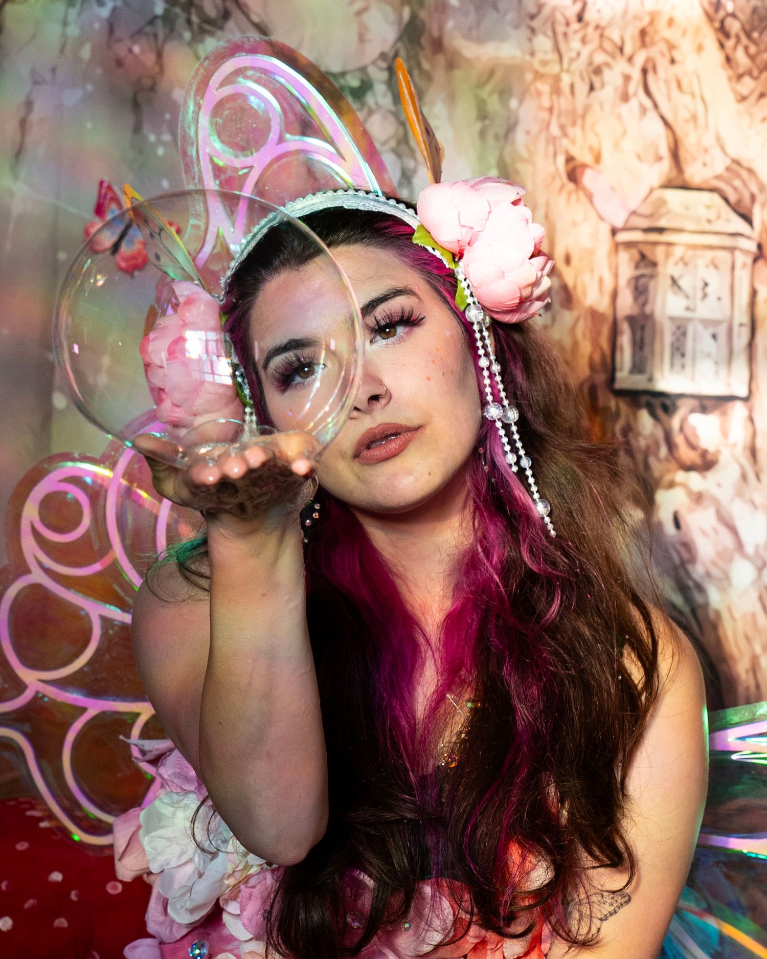 Close-up of woman in fairy costume blowing a large soap bubble in a magical enchanted forest studio. Fantasy Photoshoot