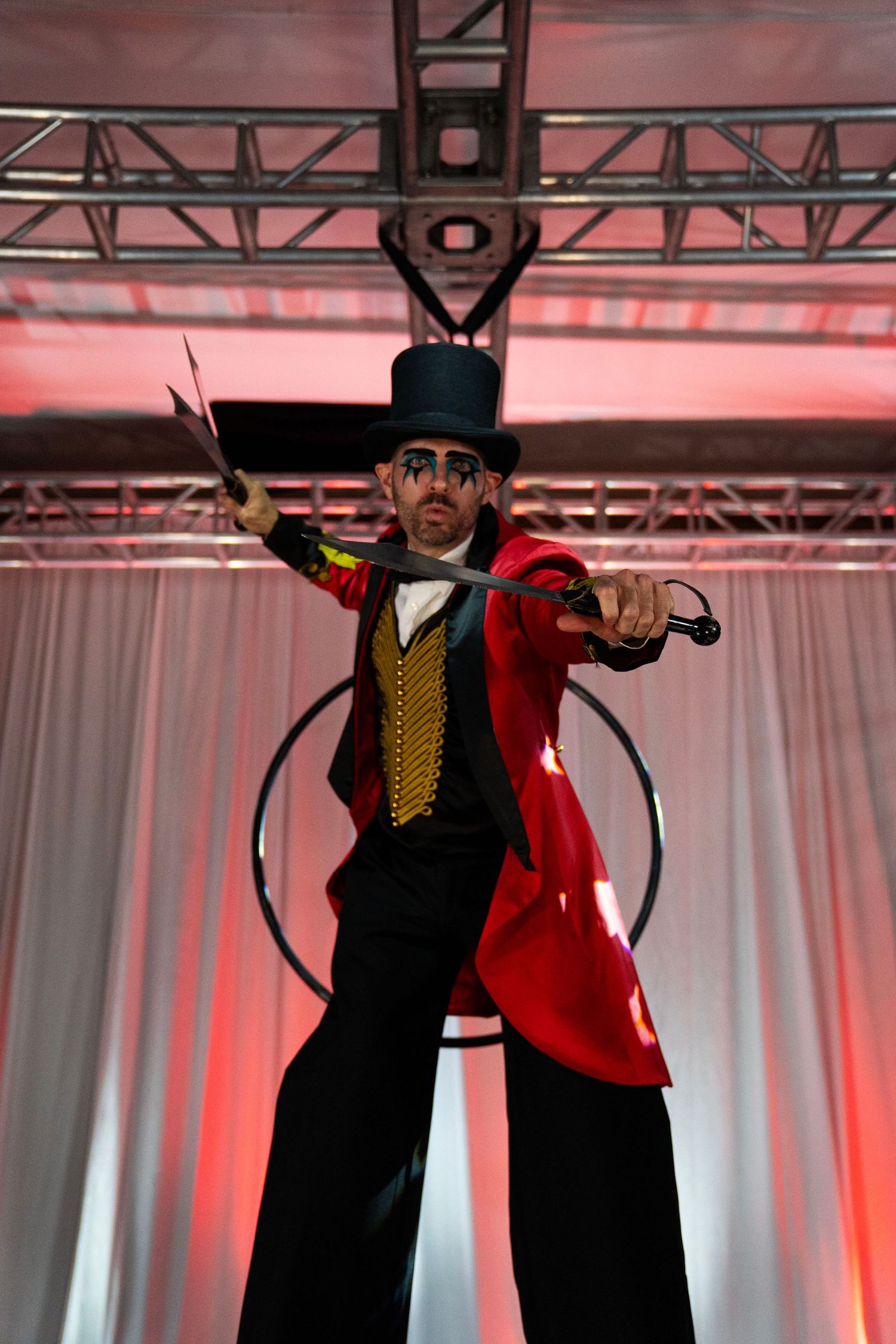 Circus ringmaster stilt walker in red coat and top hat holds sword on stage. Circus Photoshoot