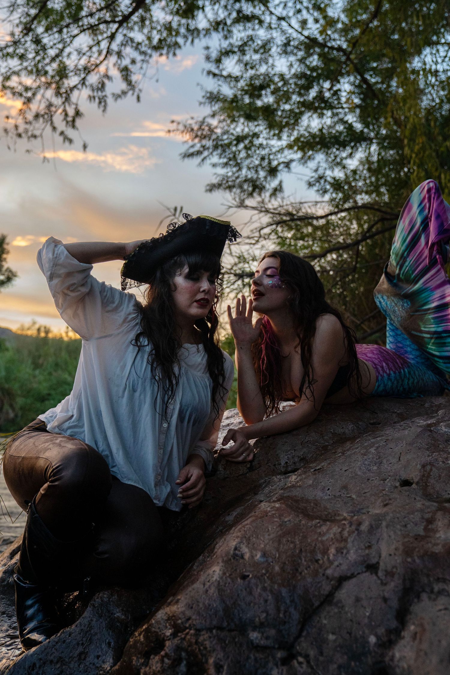 Women in pirate and mermaid costumes with dramatic makeup posing on rocks at sunset. Mermaid photoshoot, fantasy photoshoot.