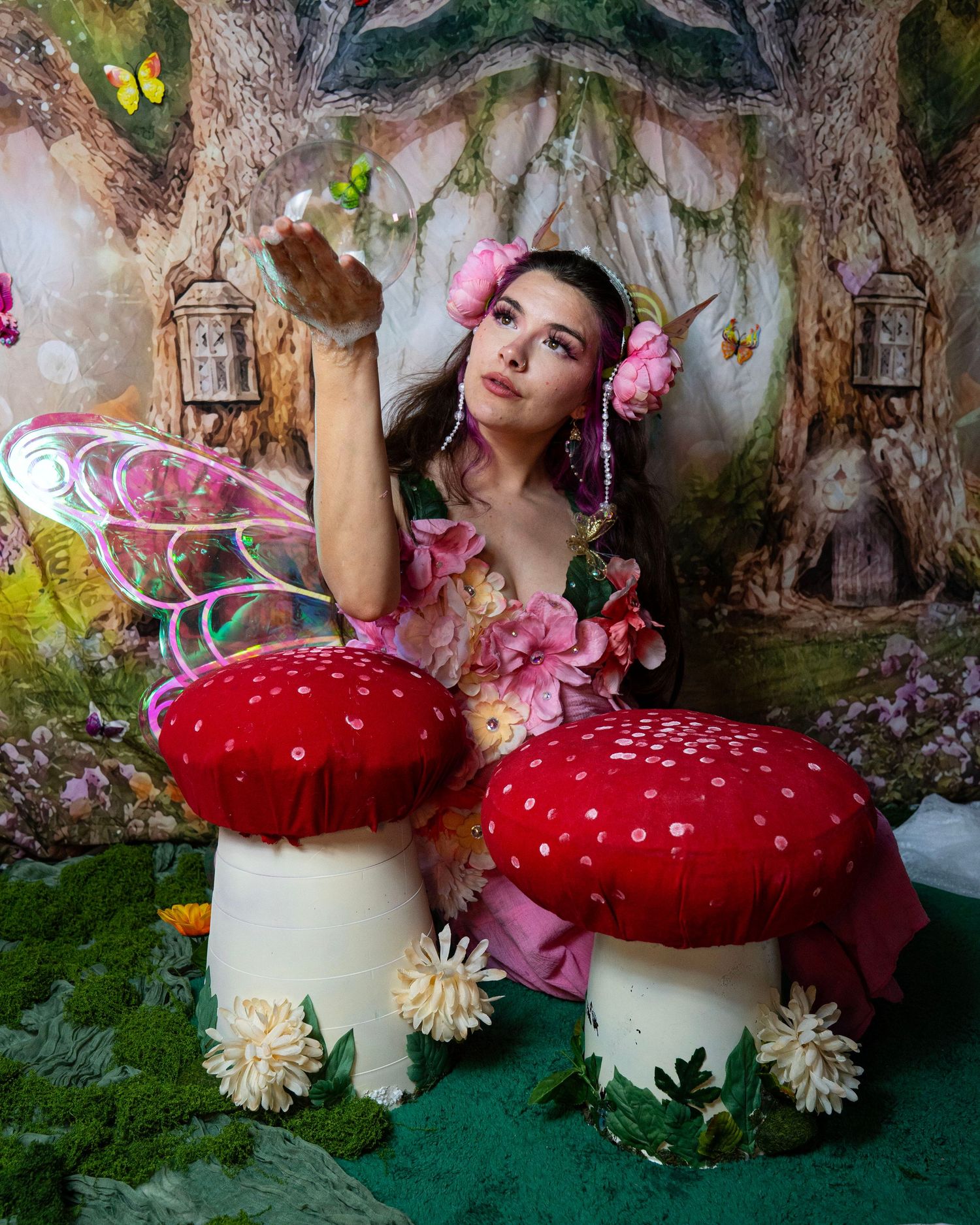 Woman dressed as a fairy with iridescent wings and floral costume reaches out in magical woodland backdrop. Fantasy Photoshoot