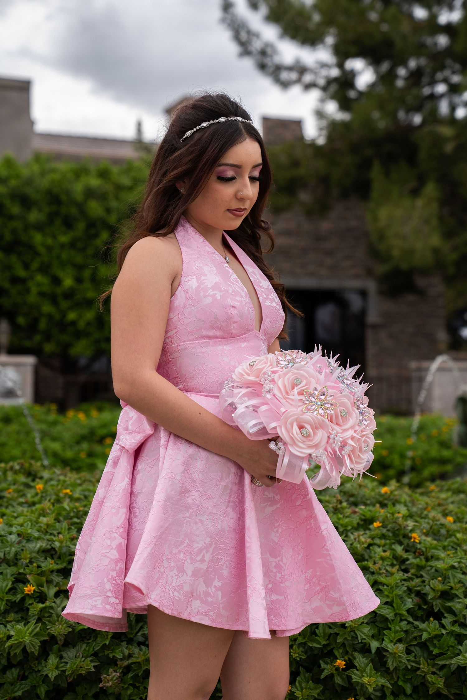 Young woman in pink halter dress holding a pink rose bouquet with jewel accents in a garden setting.
