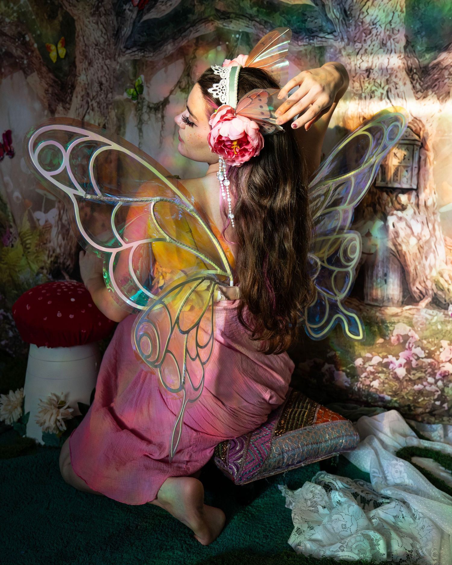 Woman in pink fairy dress with iridescent wings reaching toward lantern in enchanted forest photo studio setting. Fantasy Photoshoot