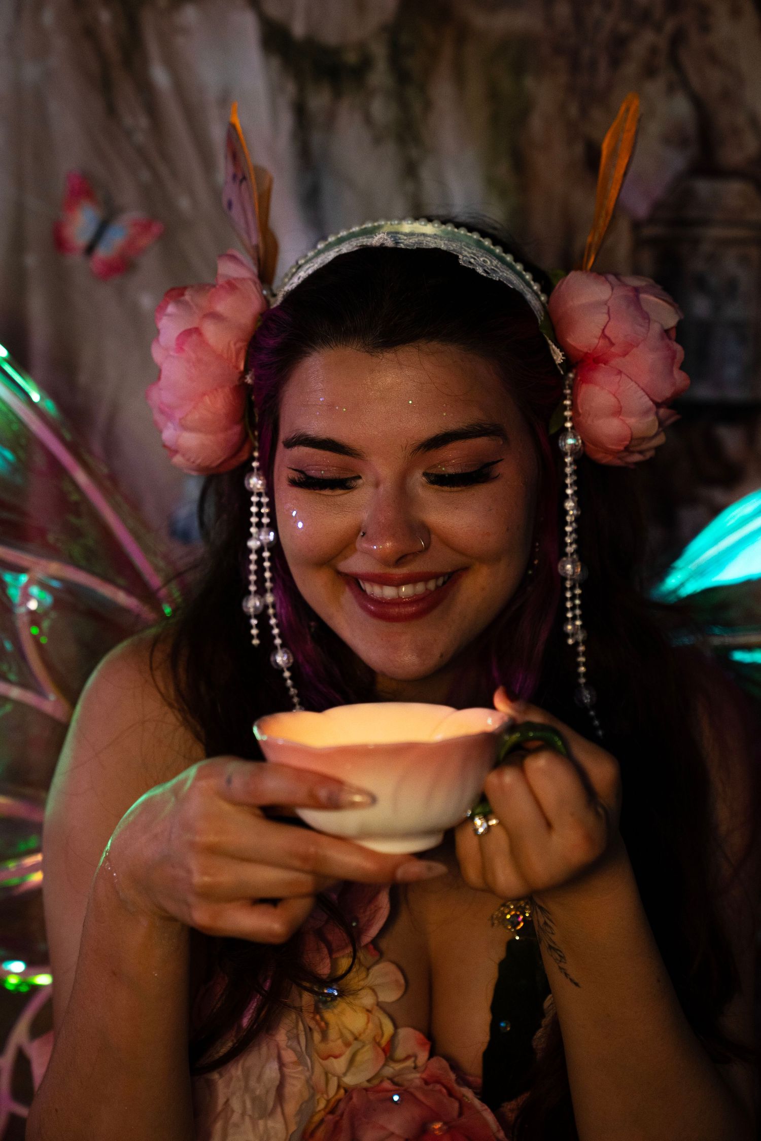 Close-up of joyful woman in floral fairy costume holding glowing lotus candle with sparkle face makeup. Fantasy Photoshoot