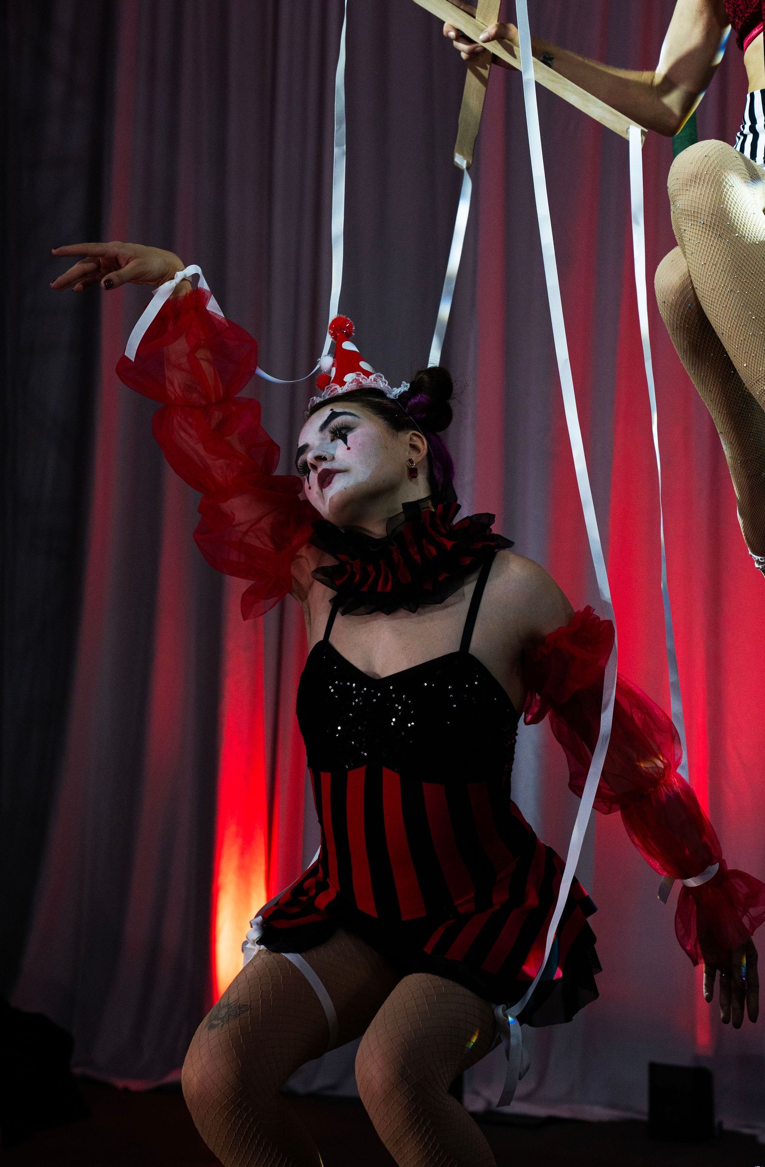 Female circus performer in clown costume with white face paint poses dramatically on stage. Circus Photoshoot