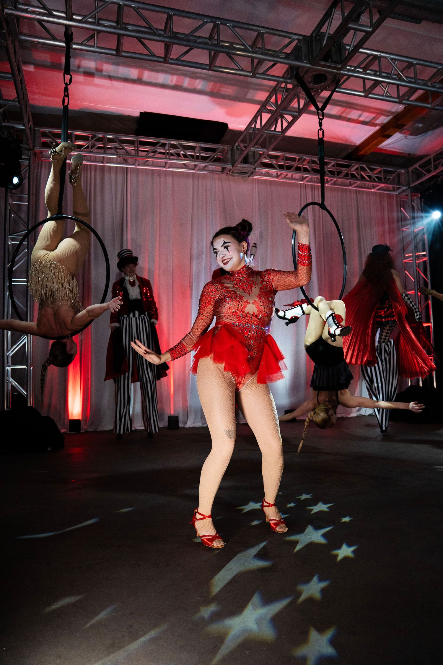 A circus performer in a red sequined costume dances on a star-projected floor at a live circus show.