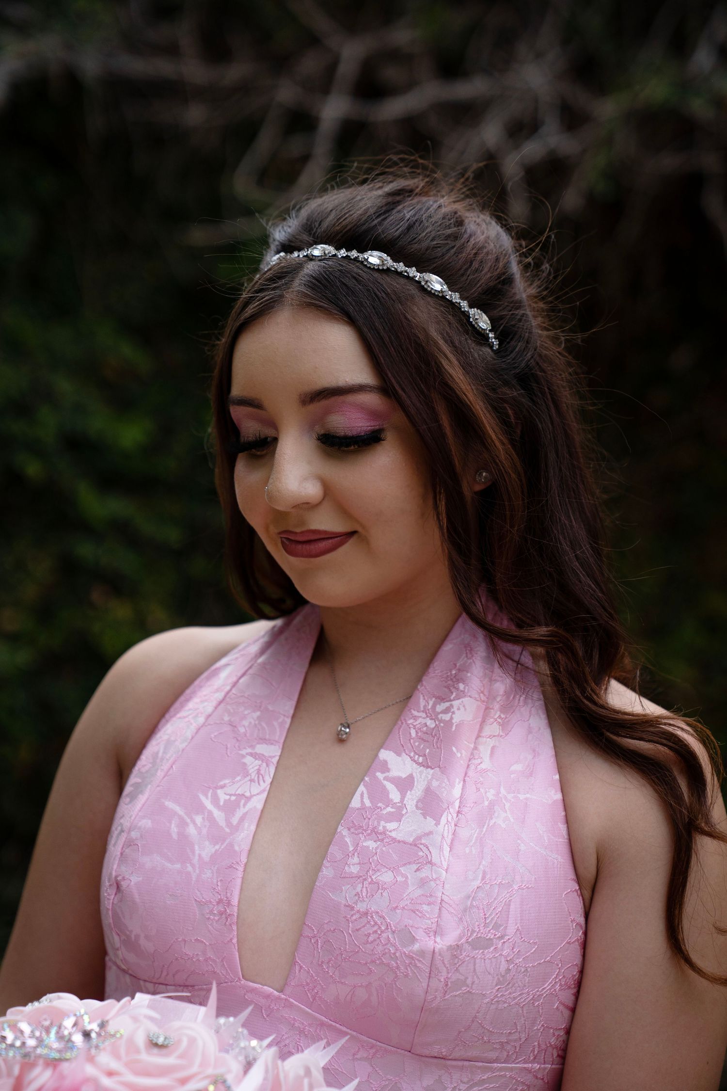 Beautiful young woman in pink lace halter dress wearing a crystal tiara with soft makeup in outdoor portrait.