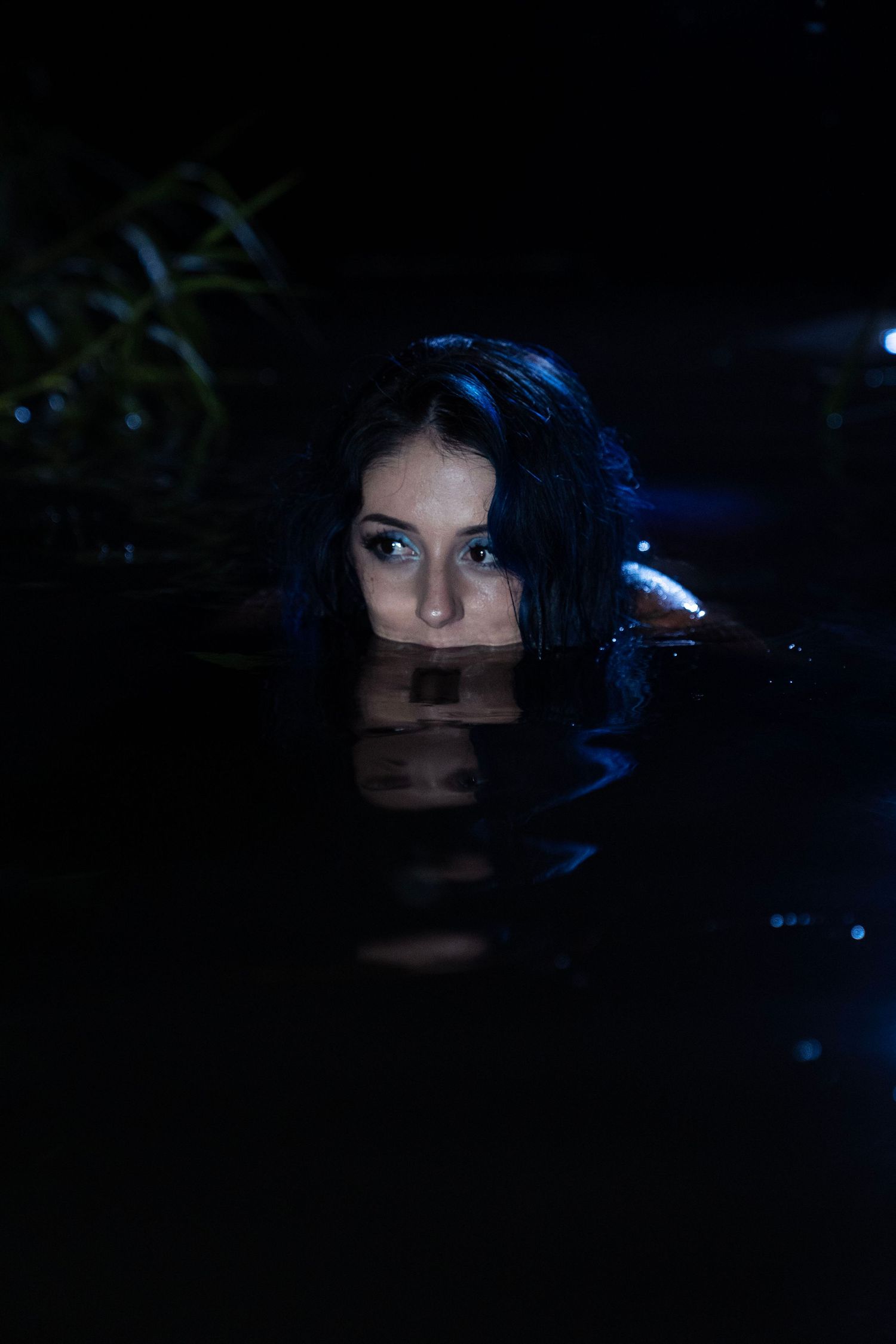Woman with dark hair submerged in dark water with only her face visible above the surface.