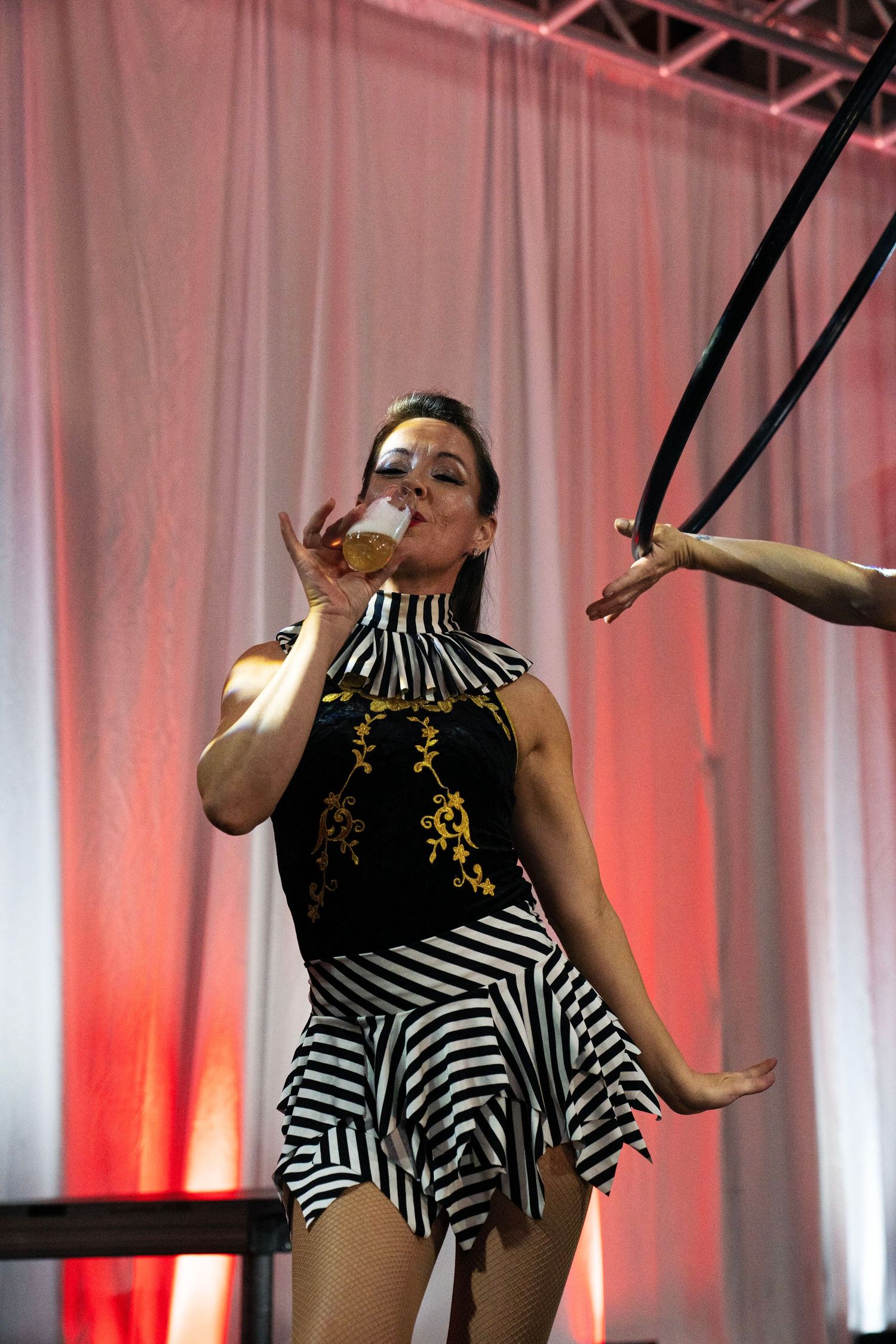 Female circus performer in black striped costume drinking from glass on stage. Circus Photoshoot