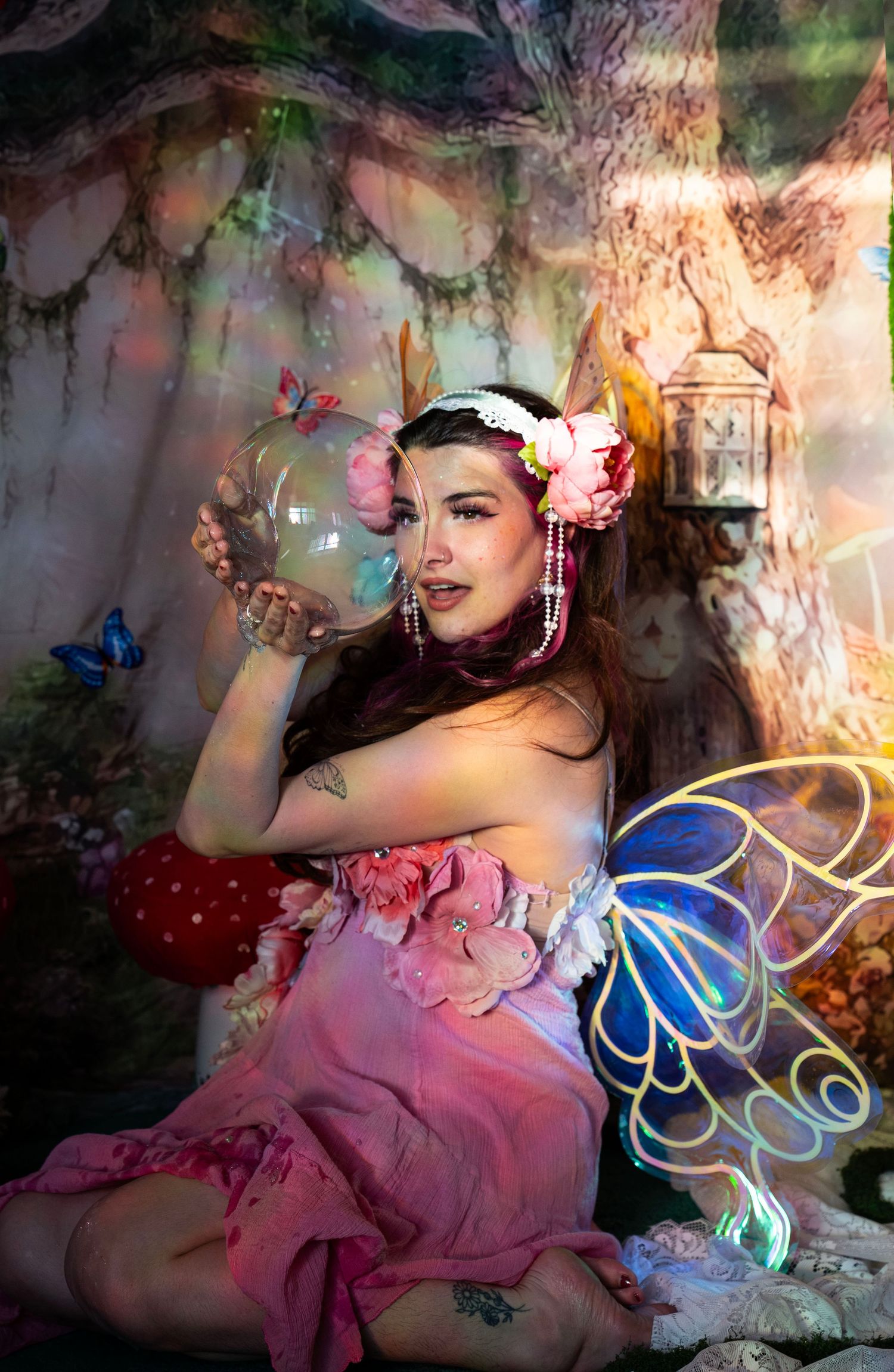 Woman in pink floral fairy costume holds a glass orb sphere in a vibrant enchanted forest studio. Fantasy Photoshoot