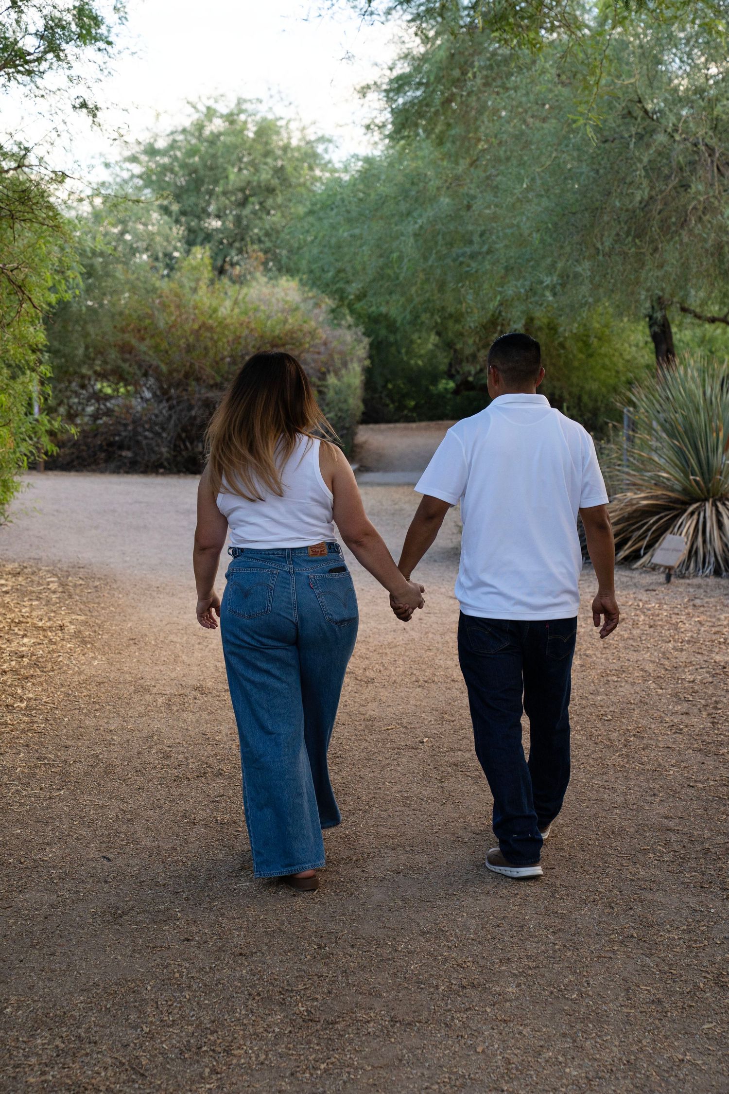 Couple holding hands walking away on a gravel path surrounded by lush desert garden greenery.