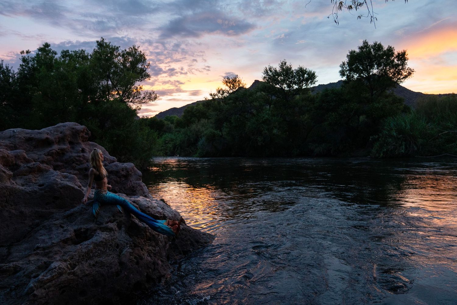 Mermaid costume model lying on rocks by a river during golden hour sunset. Mermaid photoshoot, fantasy photoshoot. Arizona photographer.