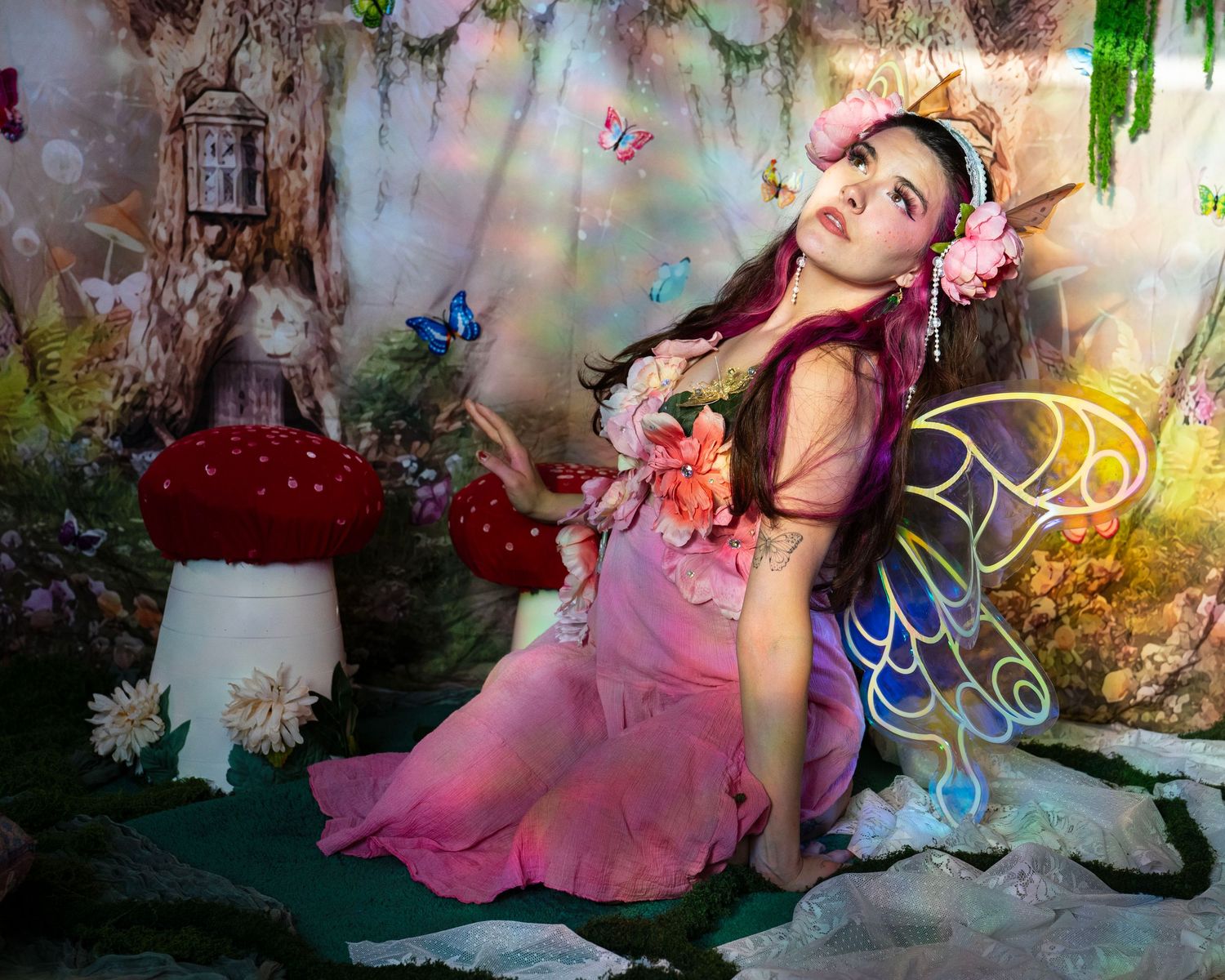 Young girl in pink fairy costume with colorful wings, flower crown, surrounded by mushrooms and butterflies in enchanted forest. Fantasy