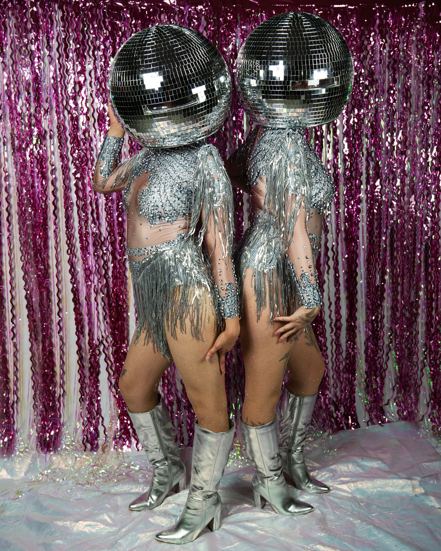 Two performers in silver rhinestone fringe costumes and disco ball helmets stand in silver boots.