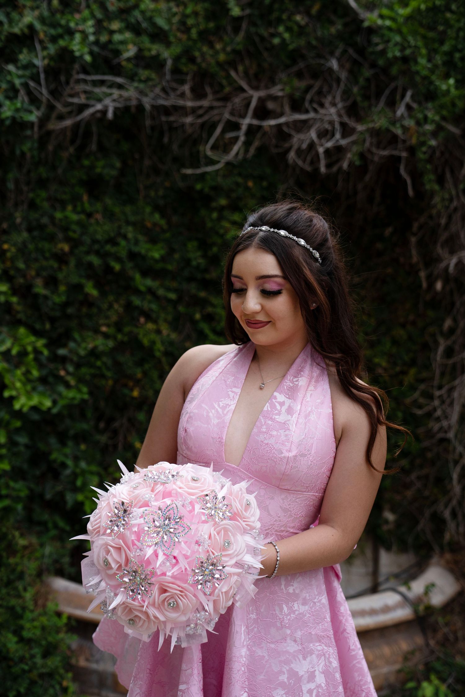 Young woman in pink halter dress holding decorative brooch bouquet with roses and feathers outdoors.