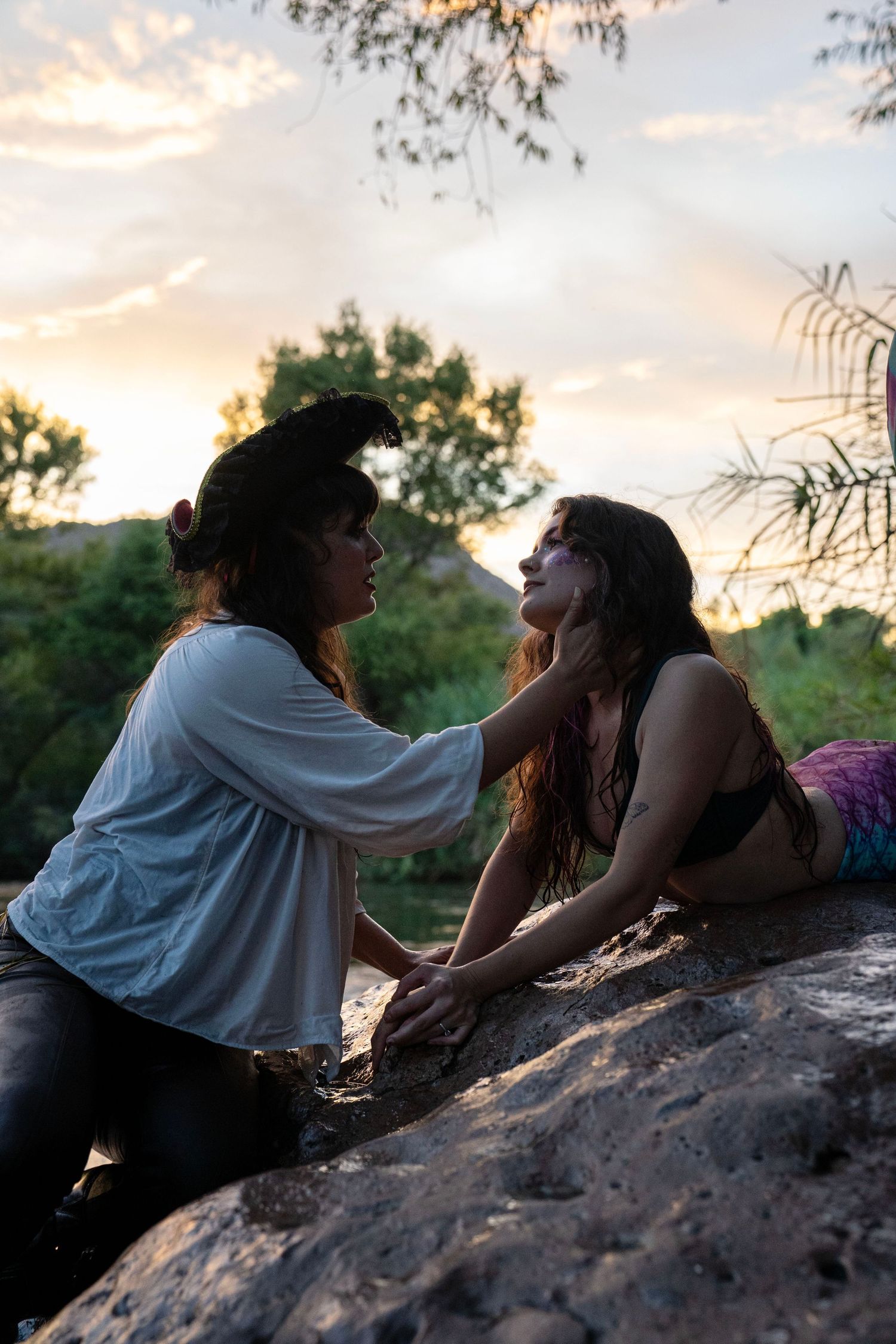 Pirate and mermaid cosplay models sharing an intimate moment on rocks during sunset. Mermaid photoshoot, fantasy photoshoot.