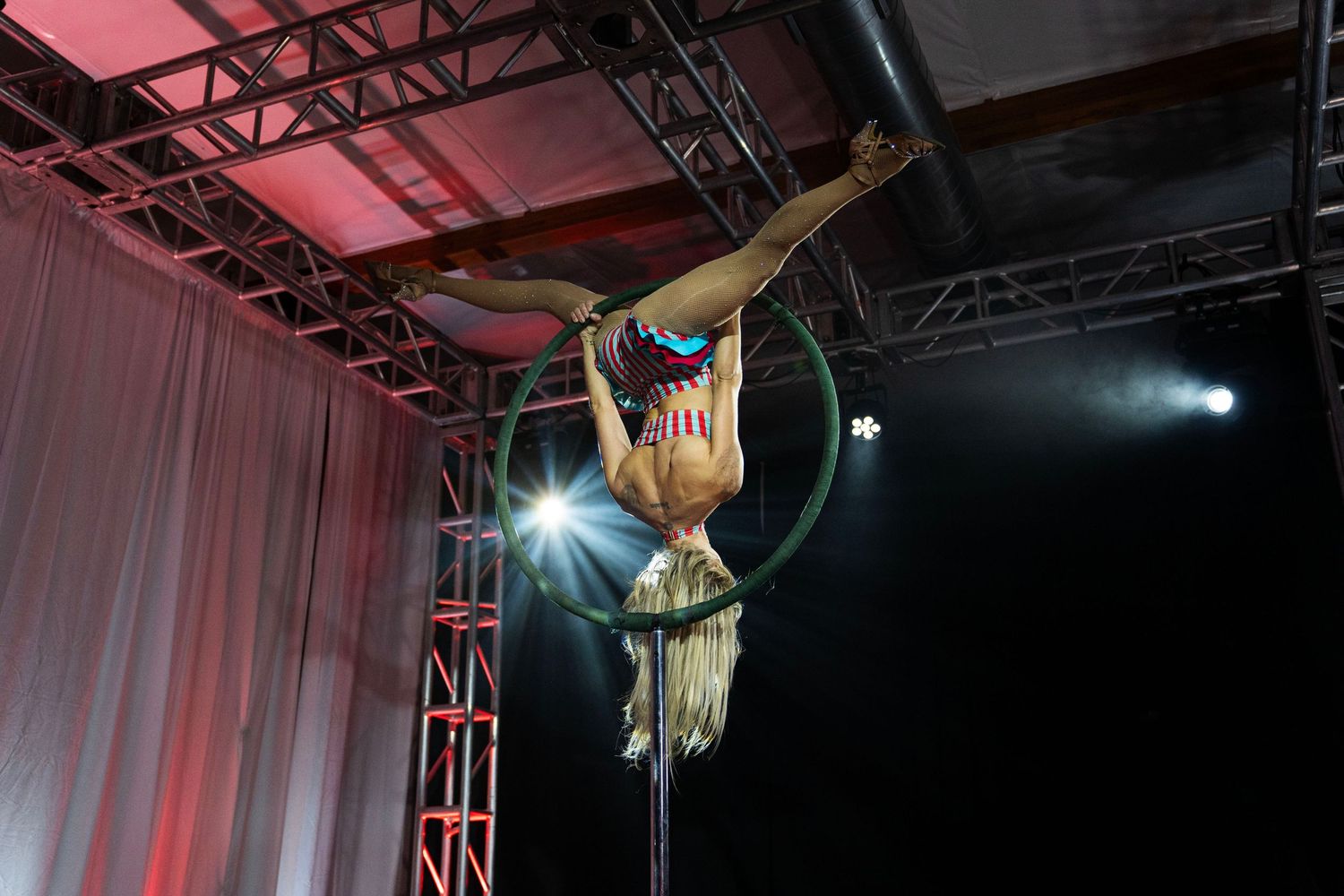 Aerial acrobat performs stunning hoop routine on pole stage with dramatic red lighting at circus performance. Circus Photoshoot