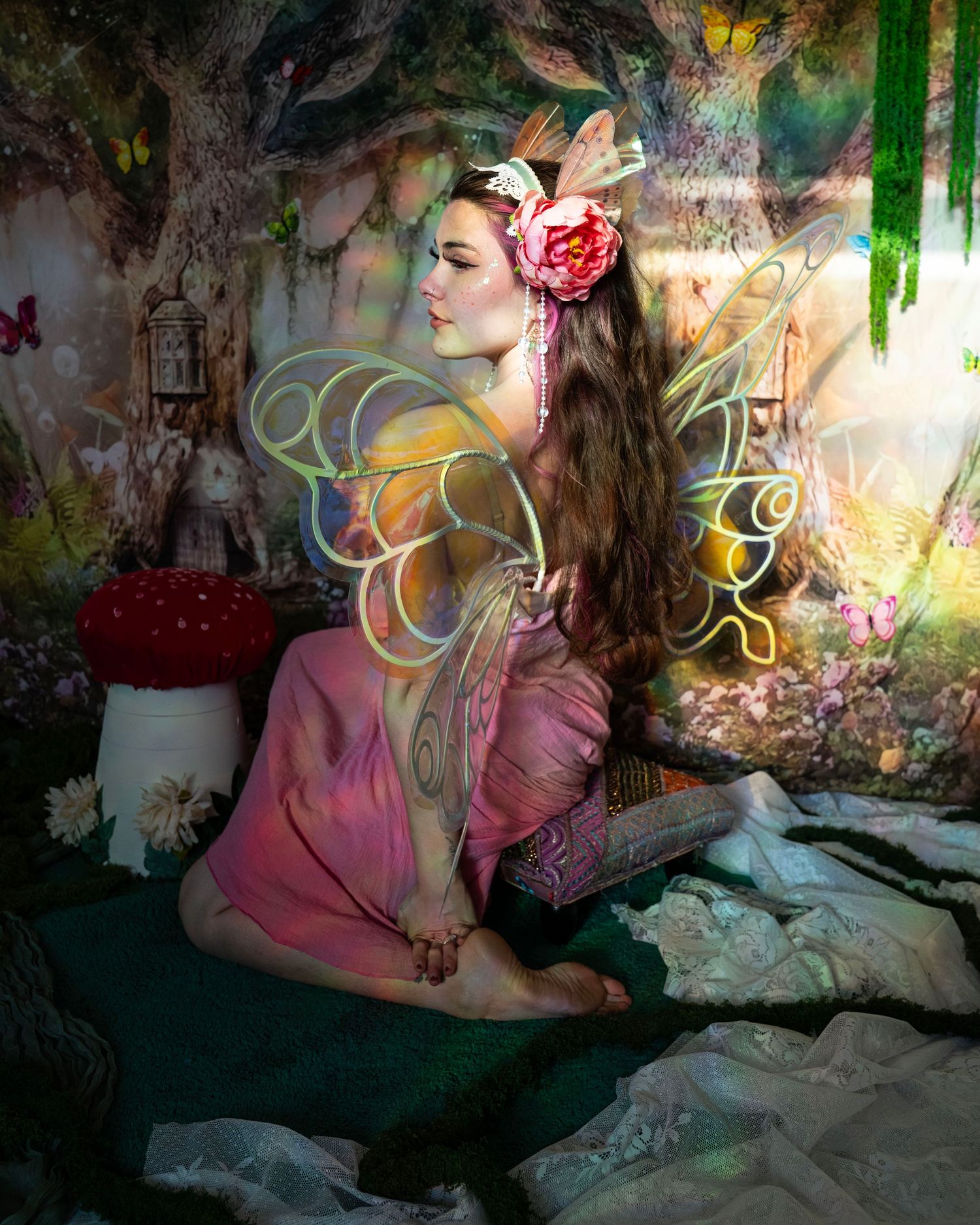 Woman with tattoos in pink fairy costume and golden wings, floral headpiece, posed in enchanted forest setting. Fantasy Photoshoot