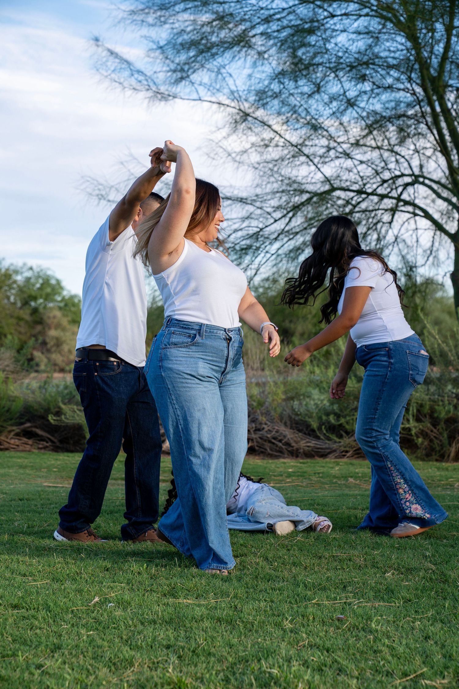 Family dancing and playing together on green grass in a park, all wearing white shirts and jeans.