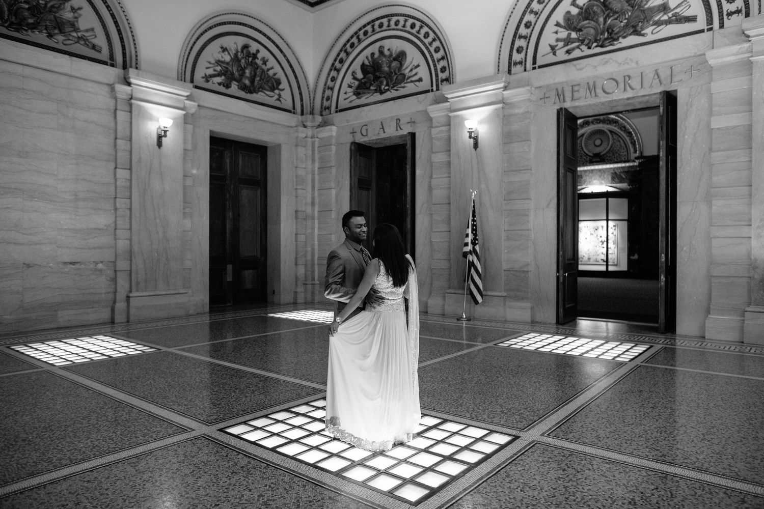 Black and white photo of couple dancing in sunlit beams in an elegant memorial hall.