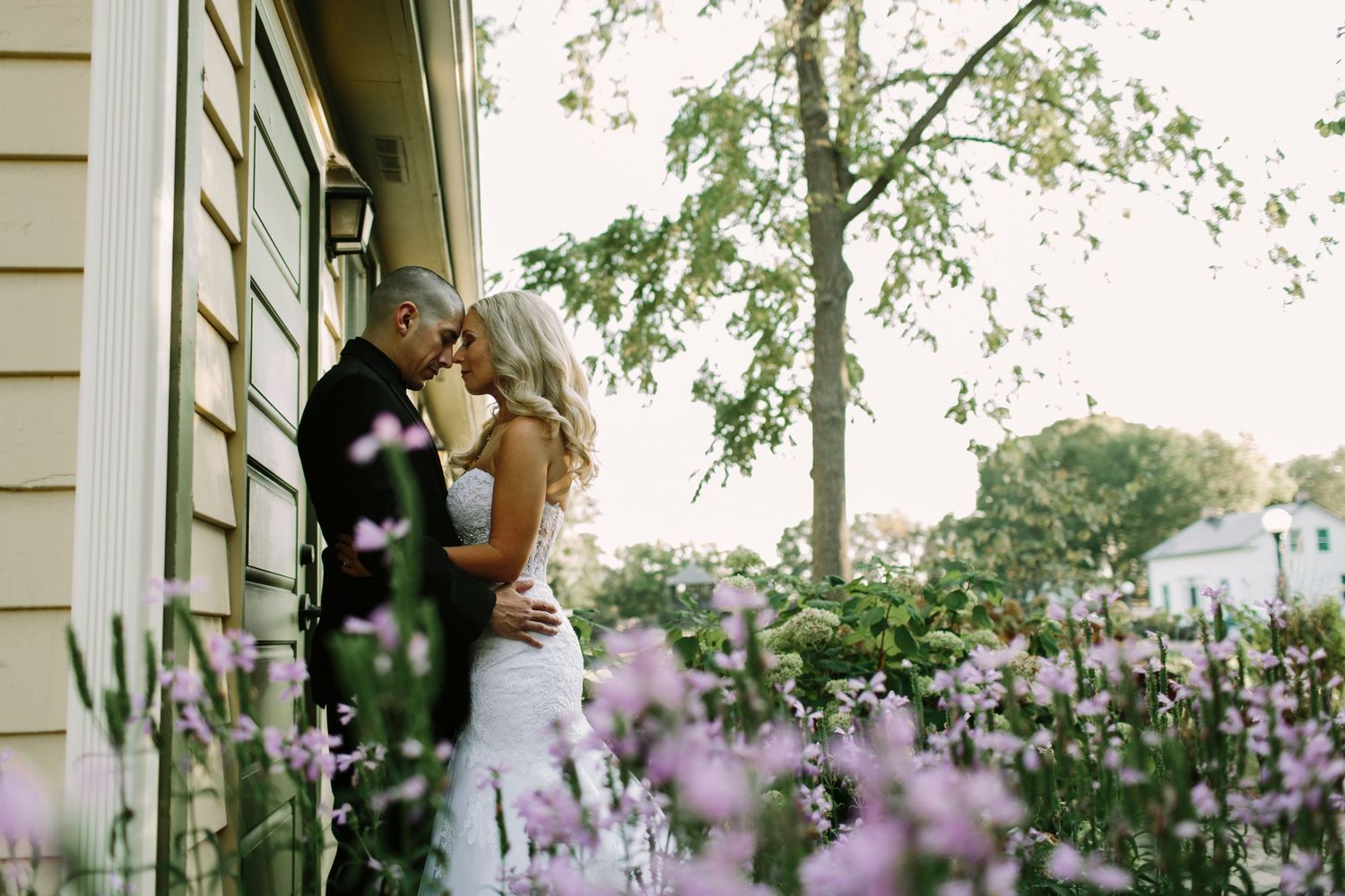 Bride and groom sharing romantic kiss surrounded by blooming purple flowers at outdoor wedding.