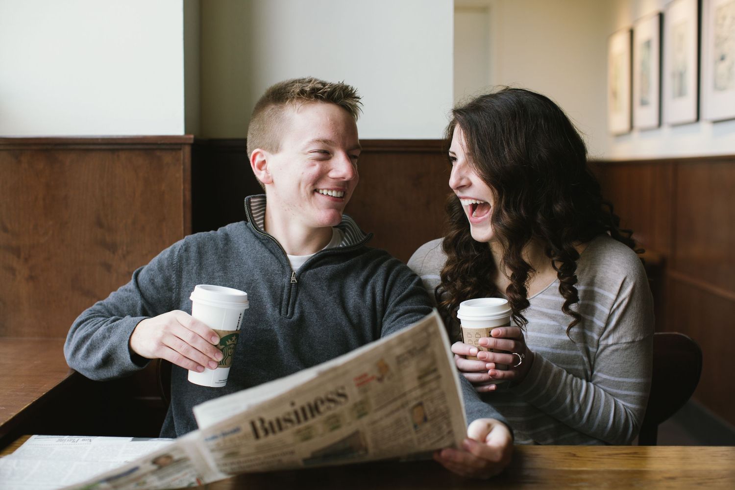 Happy couple laughing together over coffee and newspaper at a cozy cafe table.