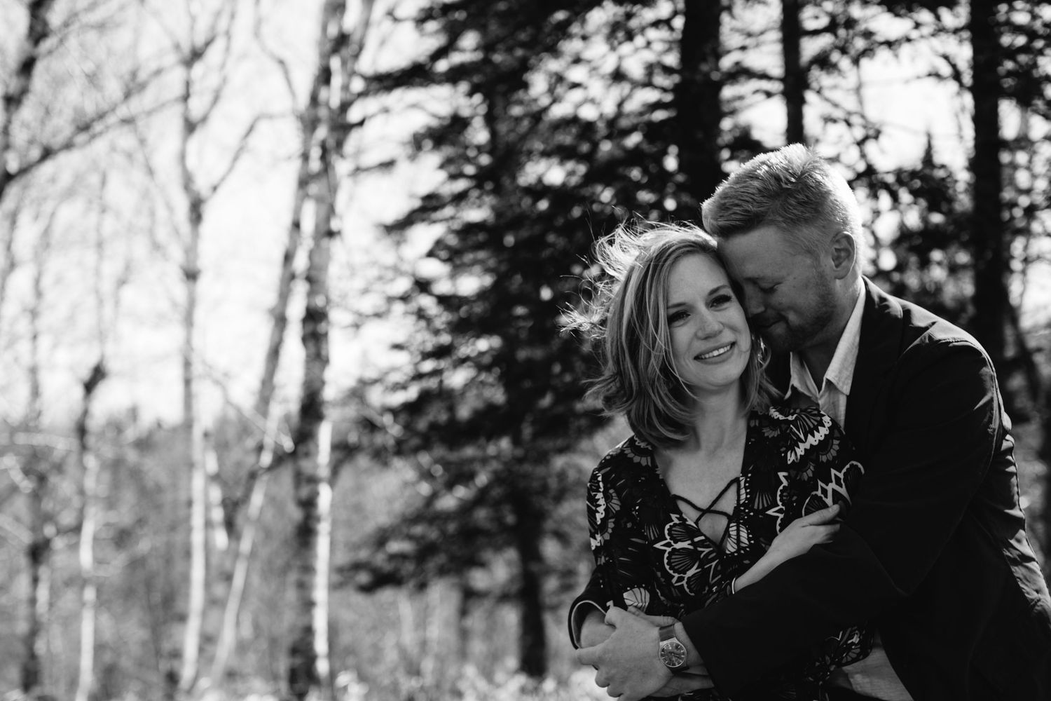 Couple embracing and laughing together in black and white forest engagement photo.