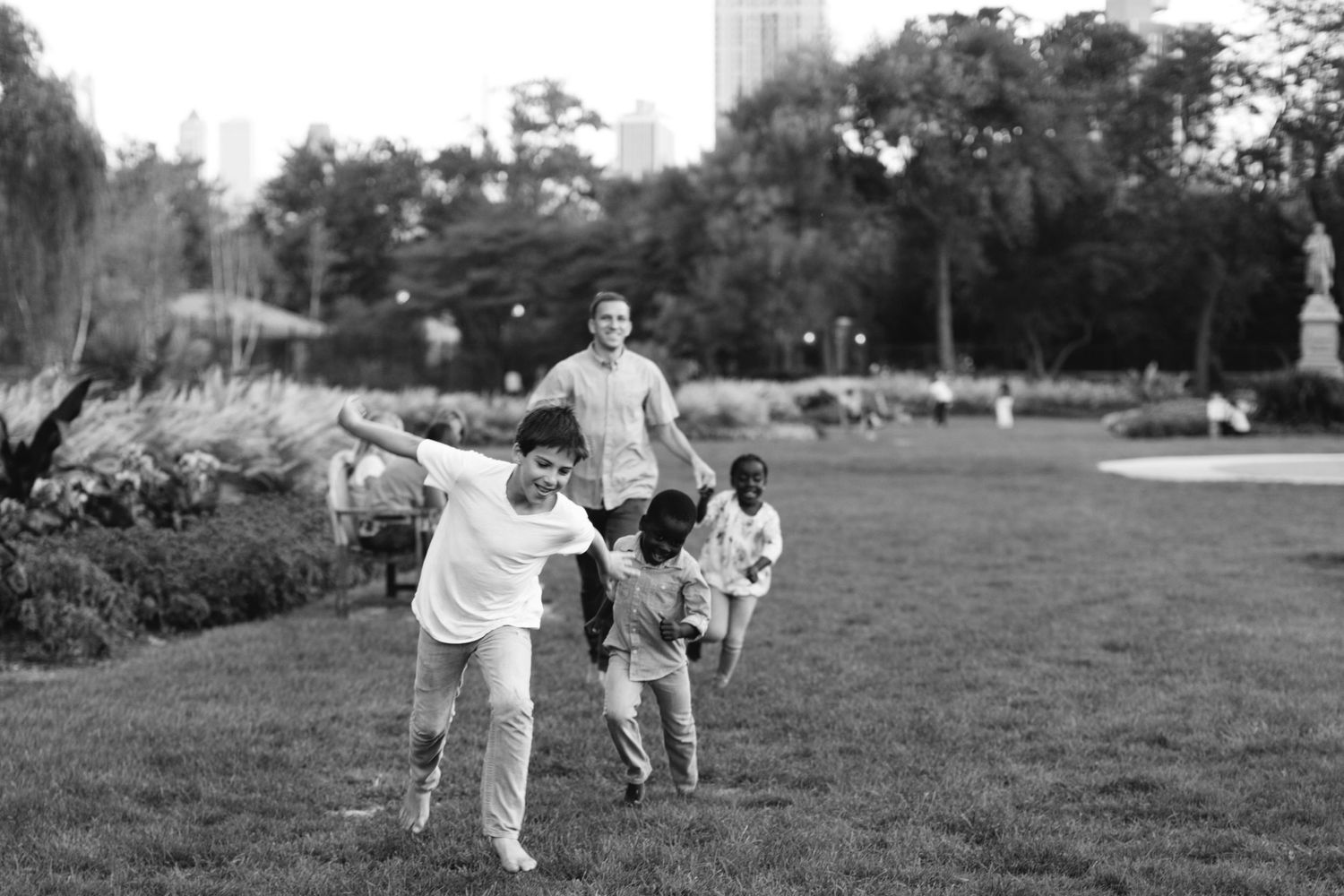 Black and white photo of children playing and running freely in a lush city park.
