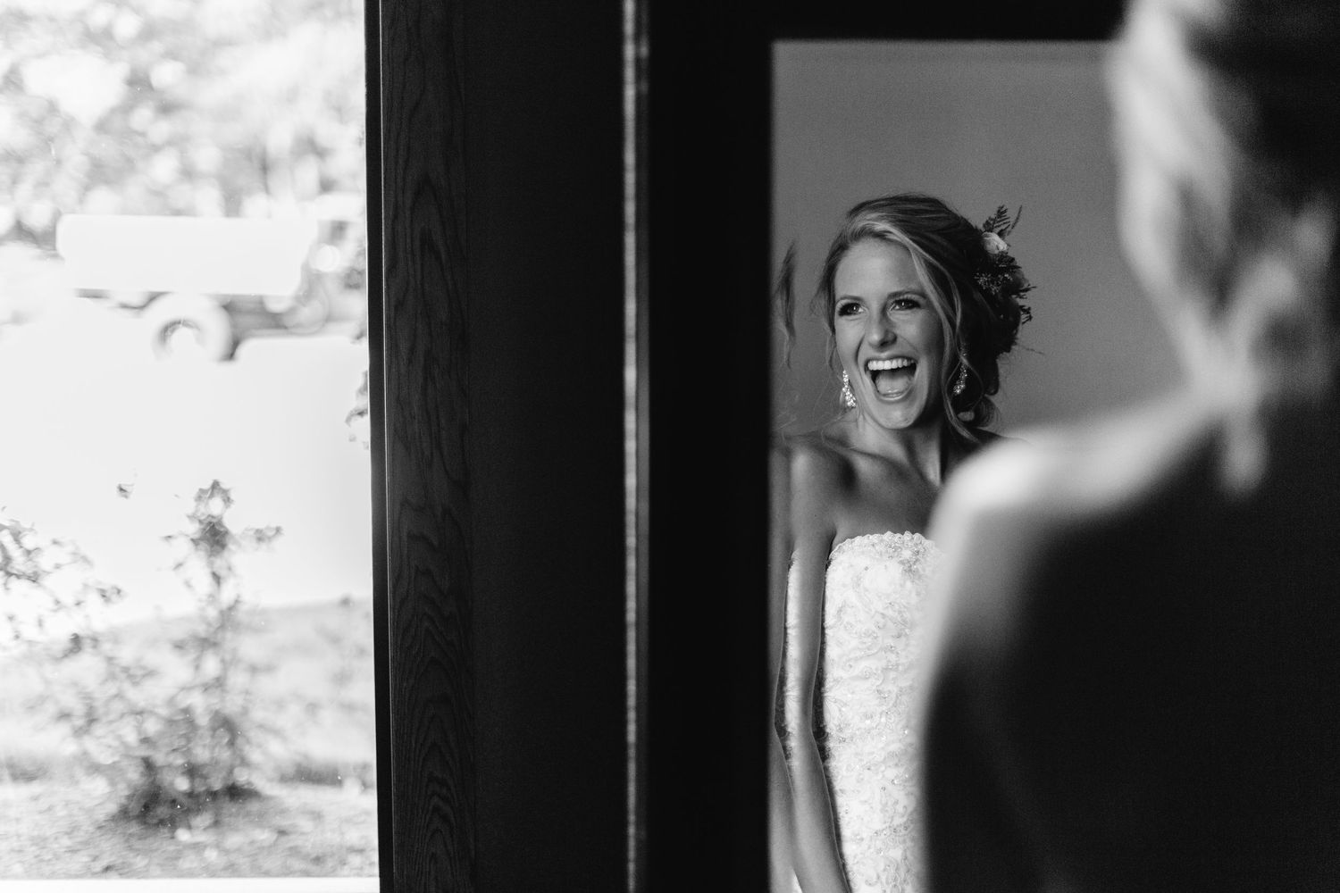 Radiant bride laughing joyfully captured in black and white mirror reflection photo.