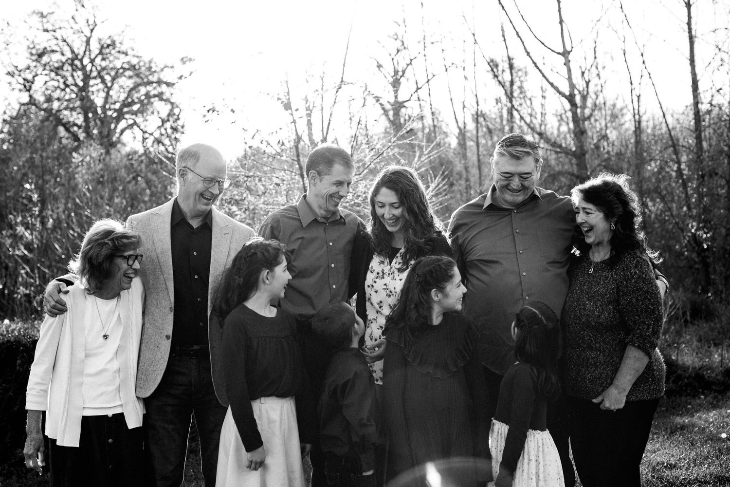 Black and white photo of a joyful multigenerational family laughing together outdoors.