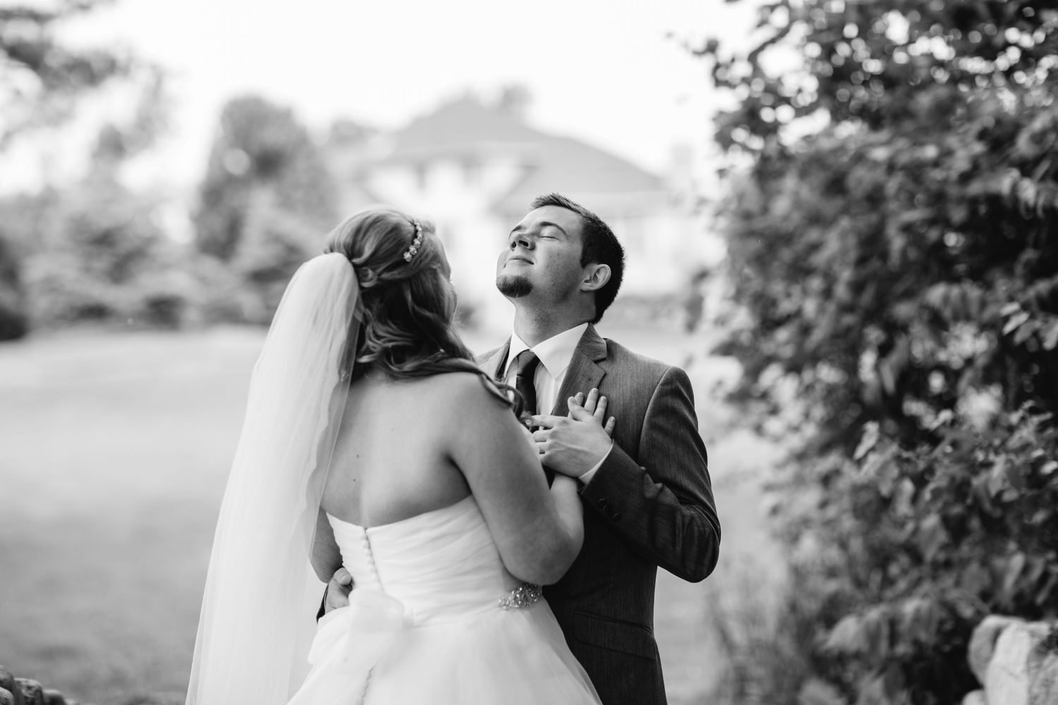 Groom gazing up emotionally during first look with bride in black and white wedding photo.