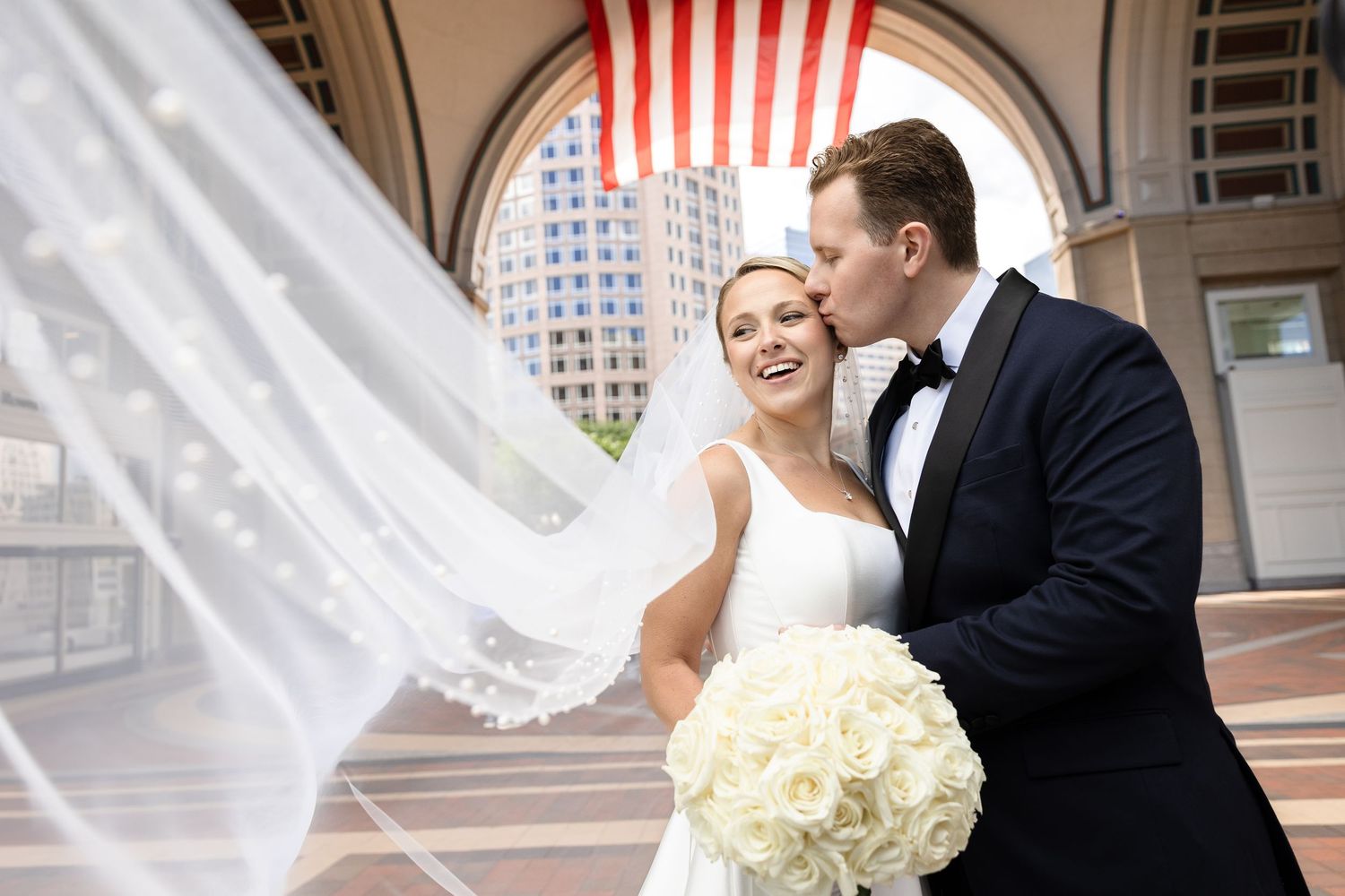 Groom kiss the bride with a flowing veil at Boston Harbor Hotel in Boston, Massachusetts, captured by Grand Photo by Karyna Oliinyk