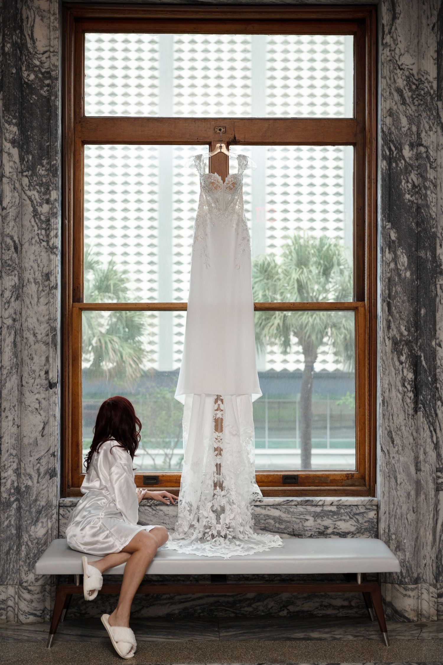 Bride admiring her wedding dress hanging in a large window at Le Méridien Tampa, Florida, captured by Grand Photo by Karyna Oliinyk