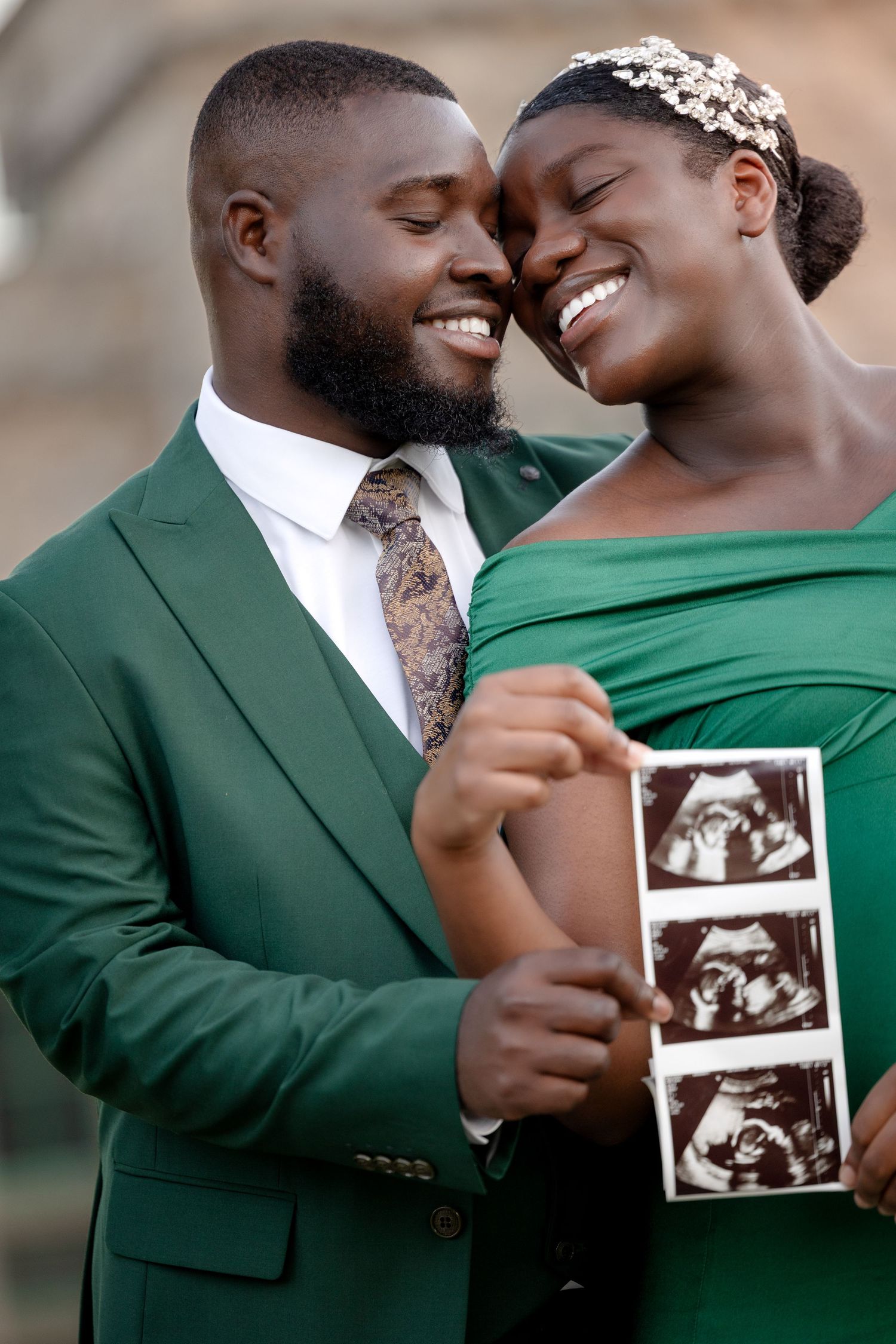 Smiling couple in green outfits holding ultrasound photos together during pregnancy announcement shoot.