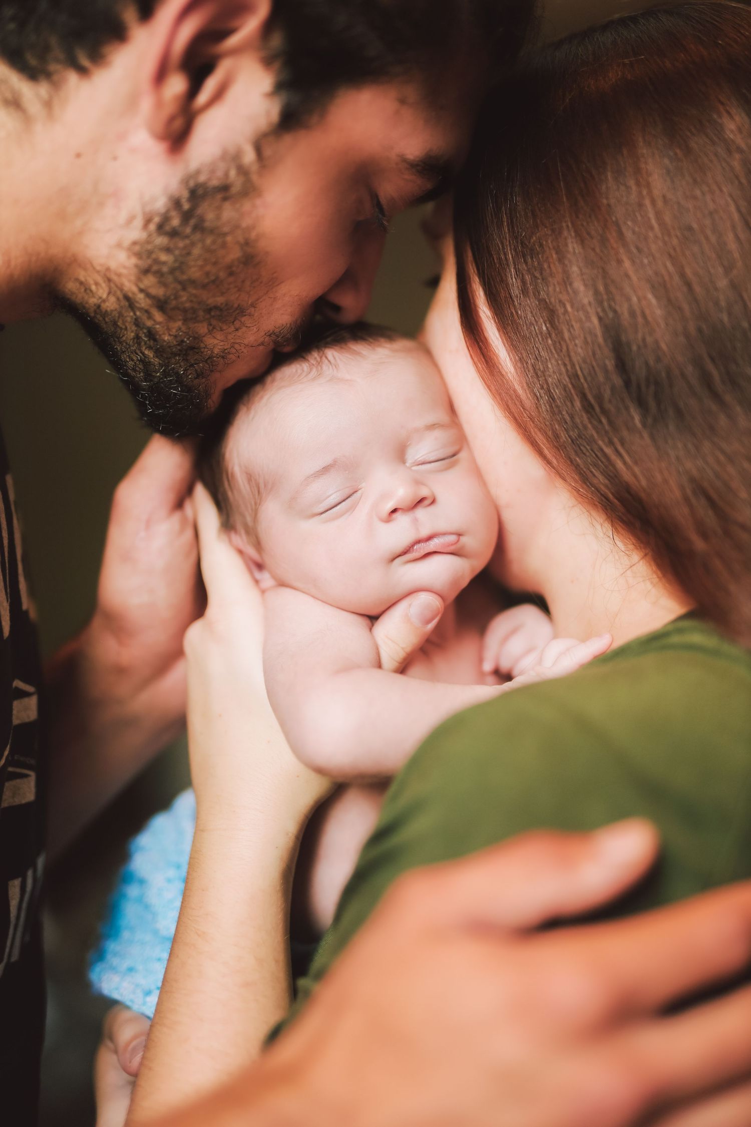 Loving parents tenderly kissing their peaceful sleeping newborn baby together in a warm embrace.