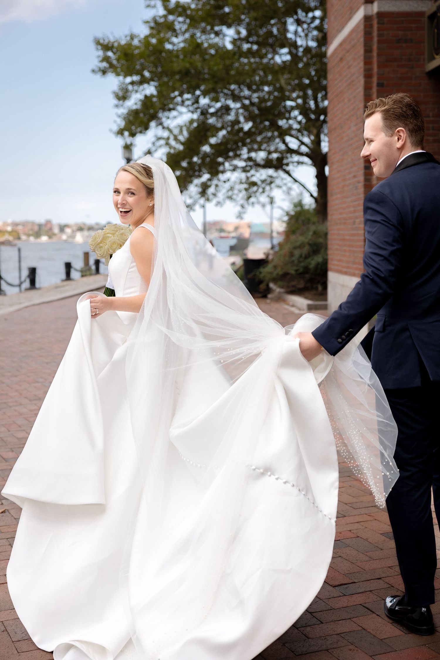 Groom carries bride’s gown at Boston Harbor Hotel in Boston, Massachusetts, captured by Grand Photo by Karyna Oliinyk
