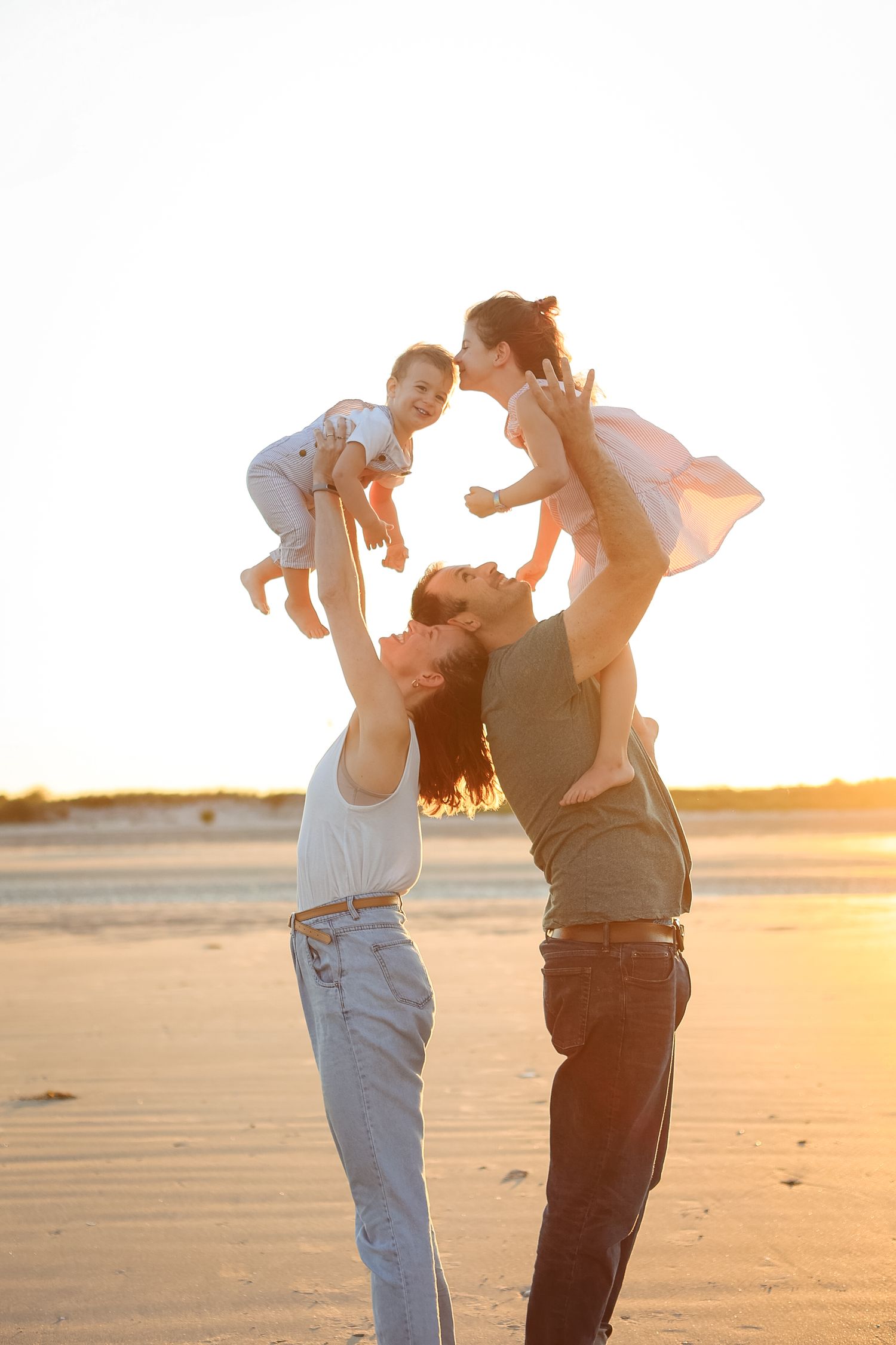 Parents joyfully lifting two young children into the air on sunny beach at golden hour.