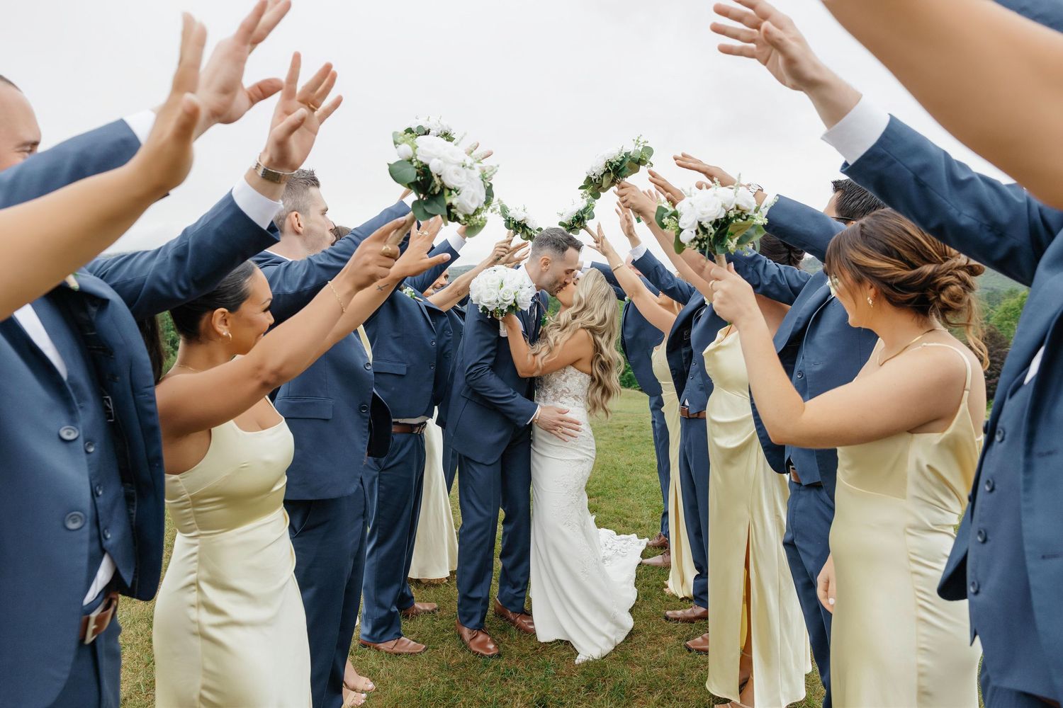 Wedding party celebrating couple kissing under floral arch at Marie Selby Botanical Gardens in Sarasota, Florida, captured by Grand Photo