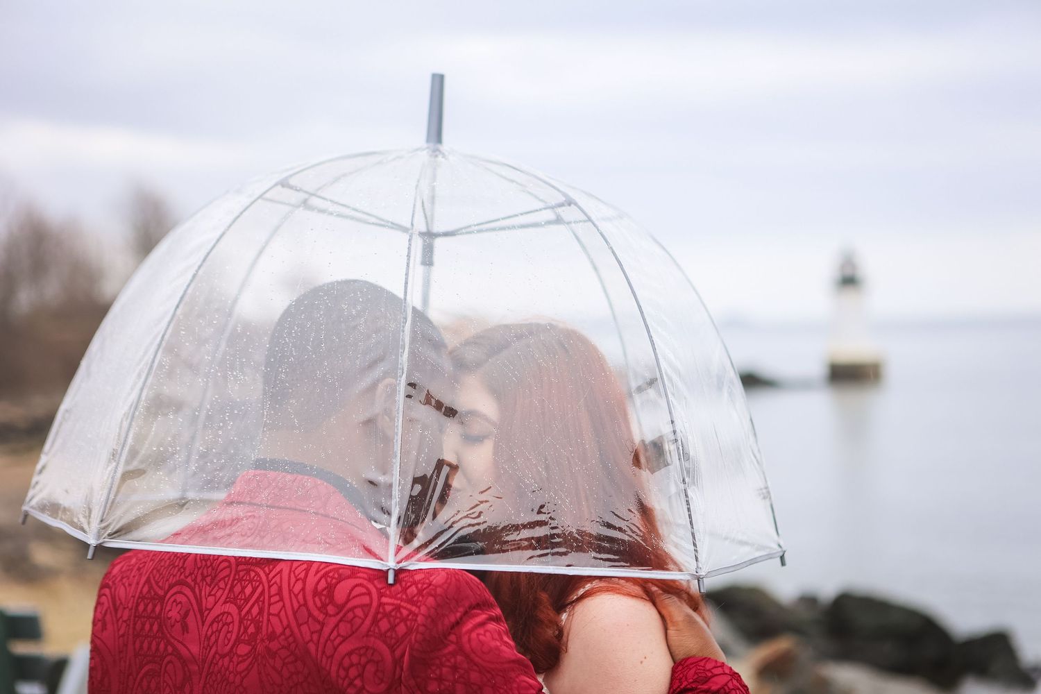 Wedding couple shares intimate kiss under transparent umbrella at Scituate Lighthouse in Scituate, Massachusetts, captured by Grand Photo