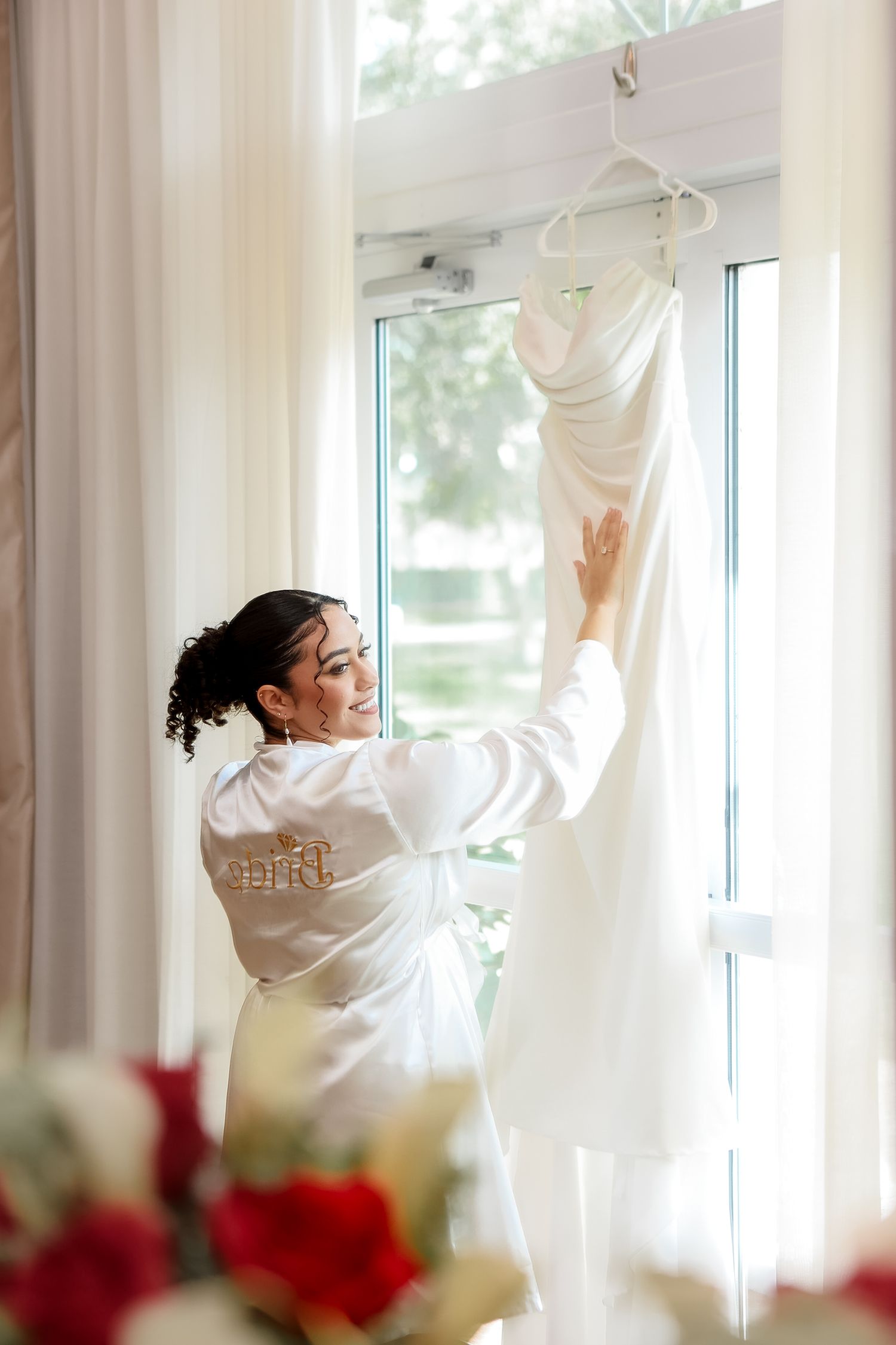 Bride in satin robe admiring her wedding gown at Harborside Chapel in Safety Harbor, Florida, captured by Grand Photo by Karyna Oliinyk